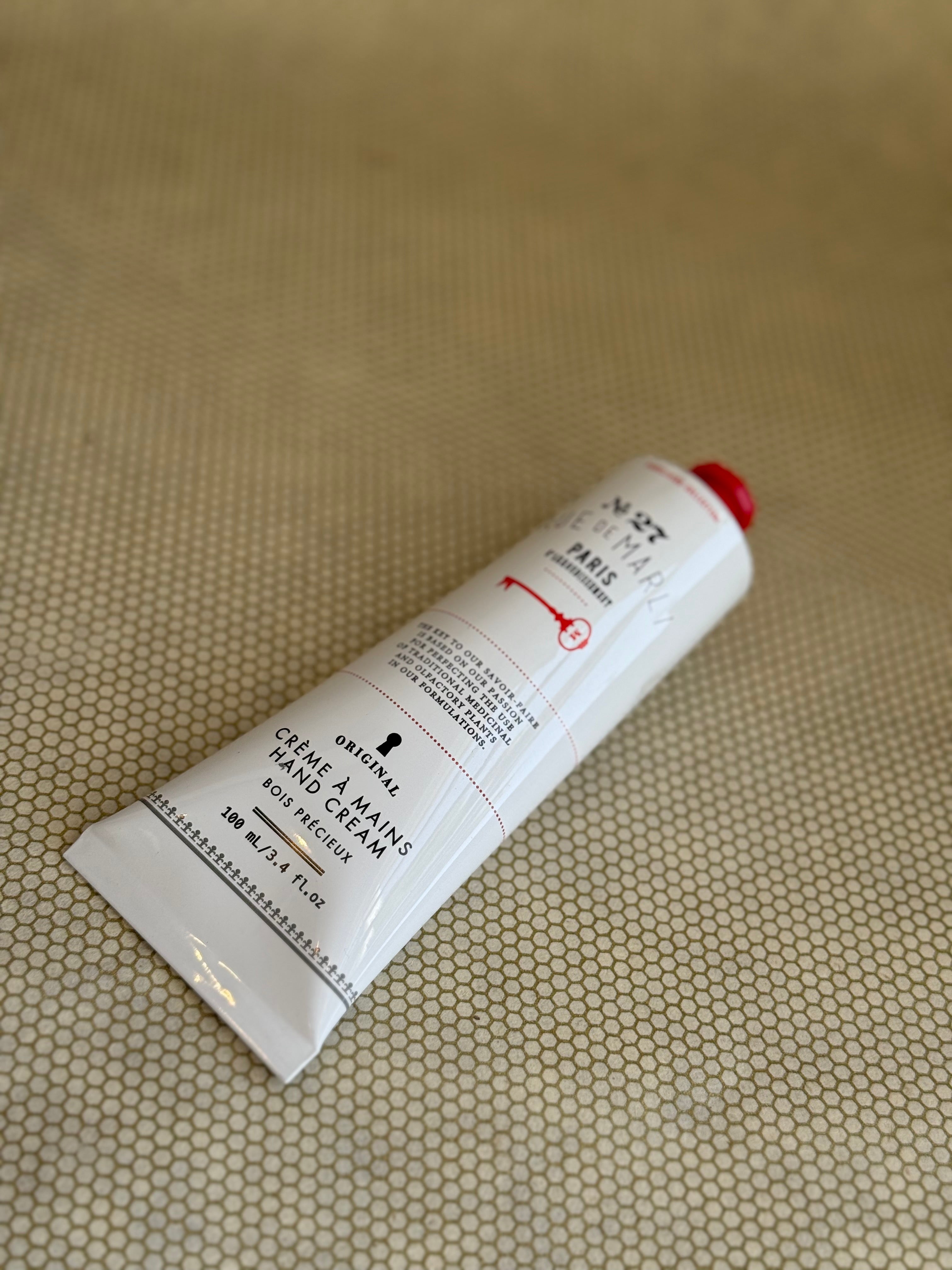 White tube of rue de marli hand cream with red cap on a beige background