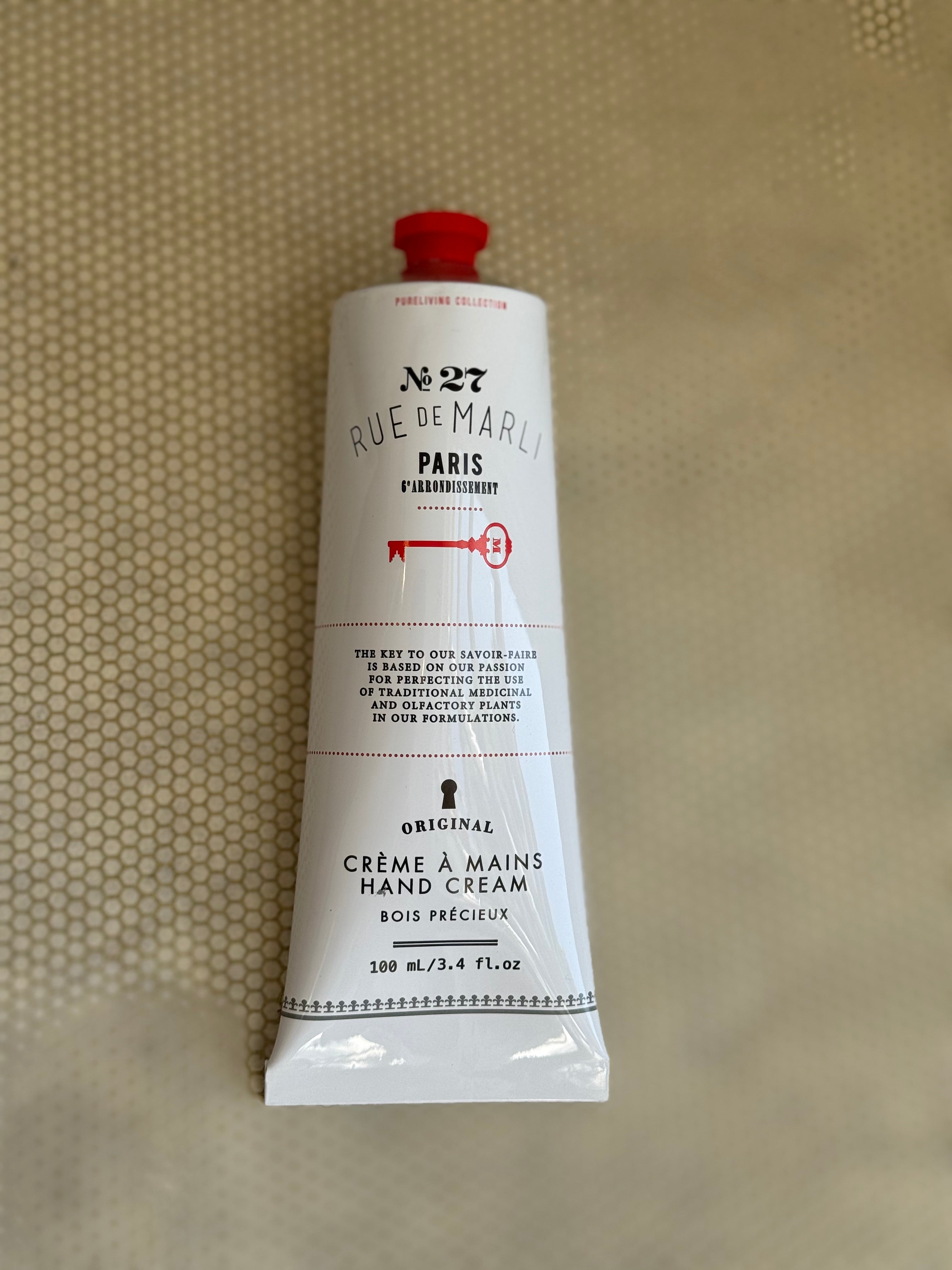 White tube of rue de marli hand cream with red cap on a beige background