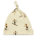 A beige organic cotton knotted baby hat with a vintage ski print, including illustrations of skiers and ski equipment.