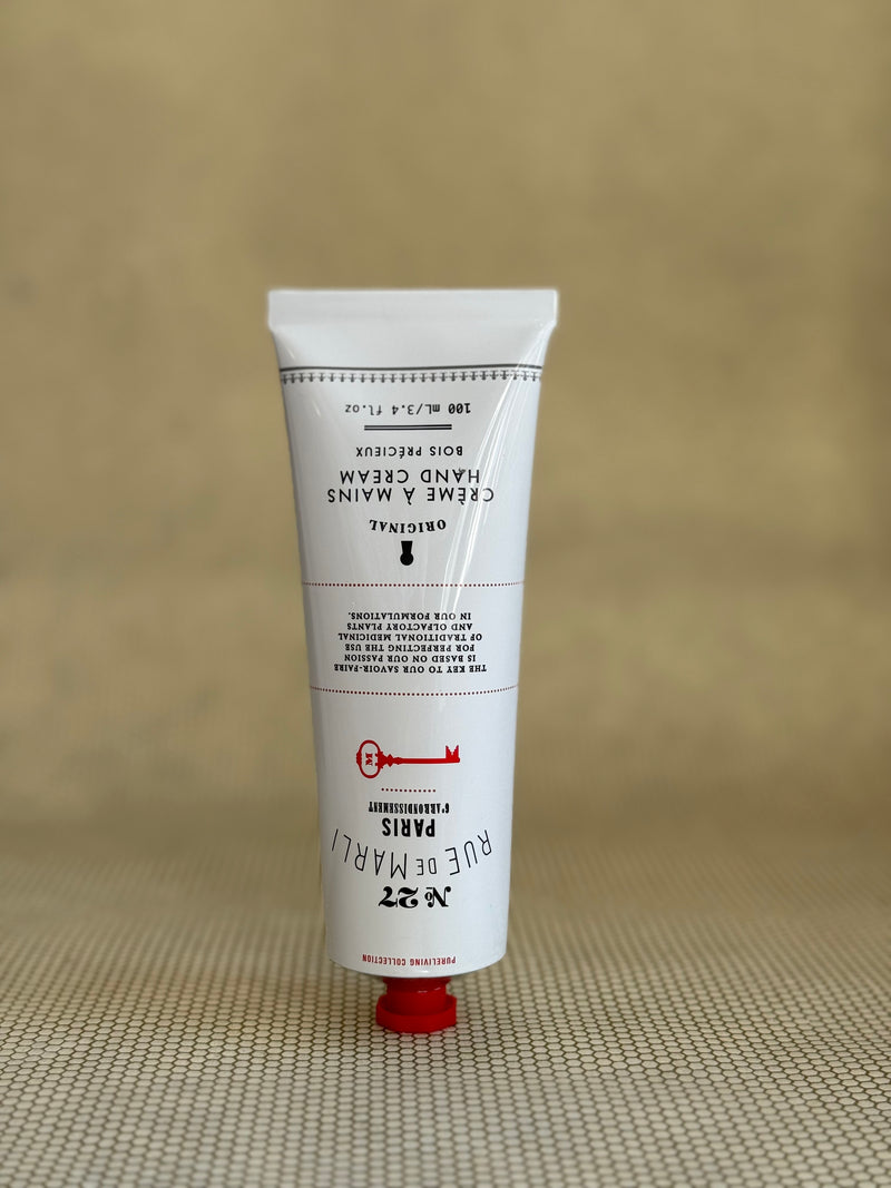 White tube of rue de marli hand cream with red cap on a beige background