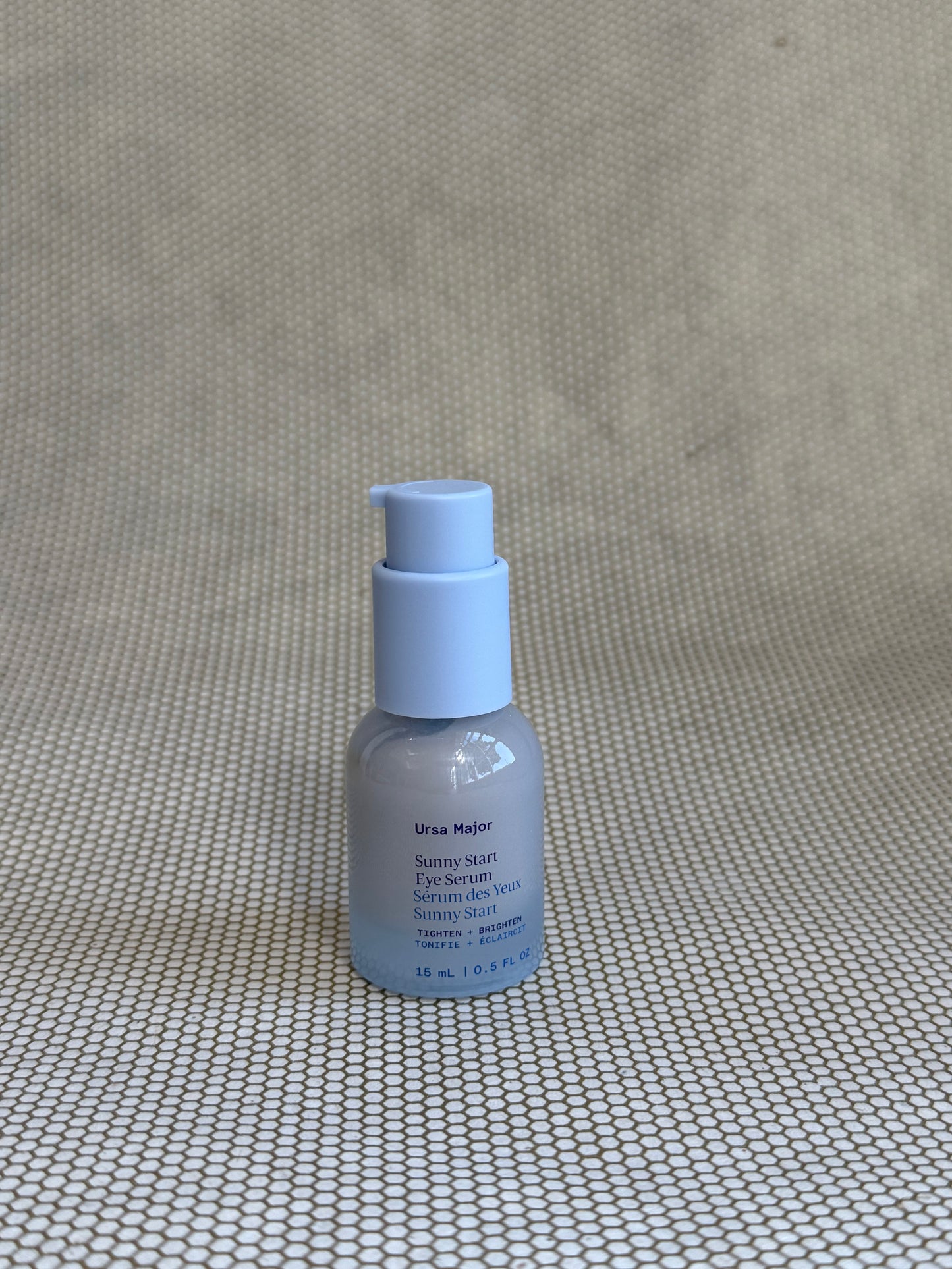 small light blue pump bottle of Ursa Major Sunny Start Eye Serum on neutral background. 