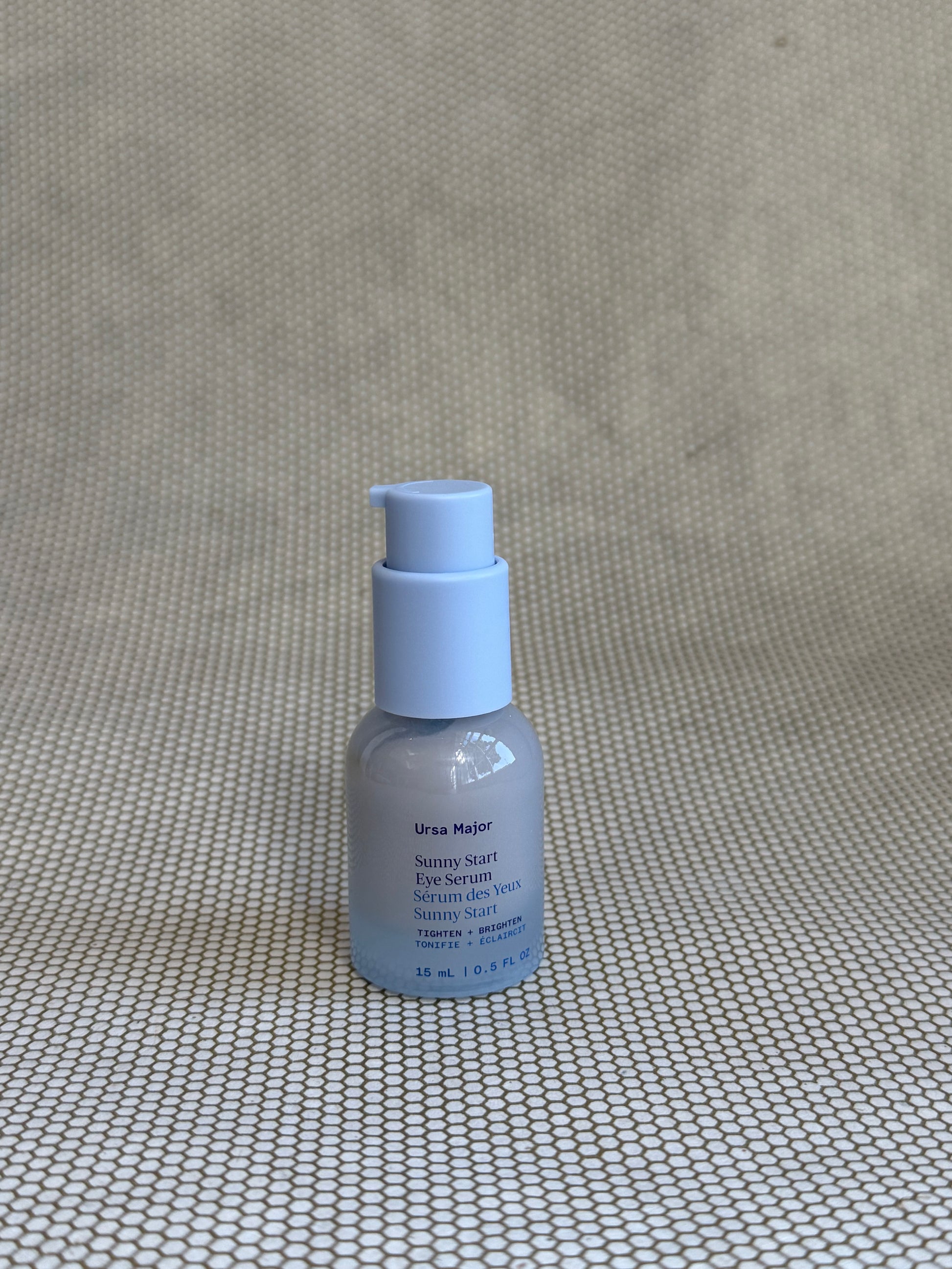 small light blue pump bottle of Ursa Major Sunny Start Eye Serum on neutral background. 