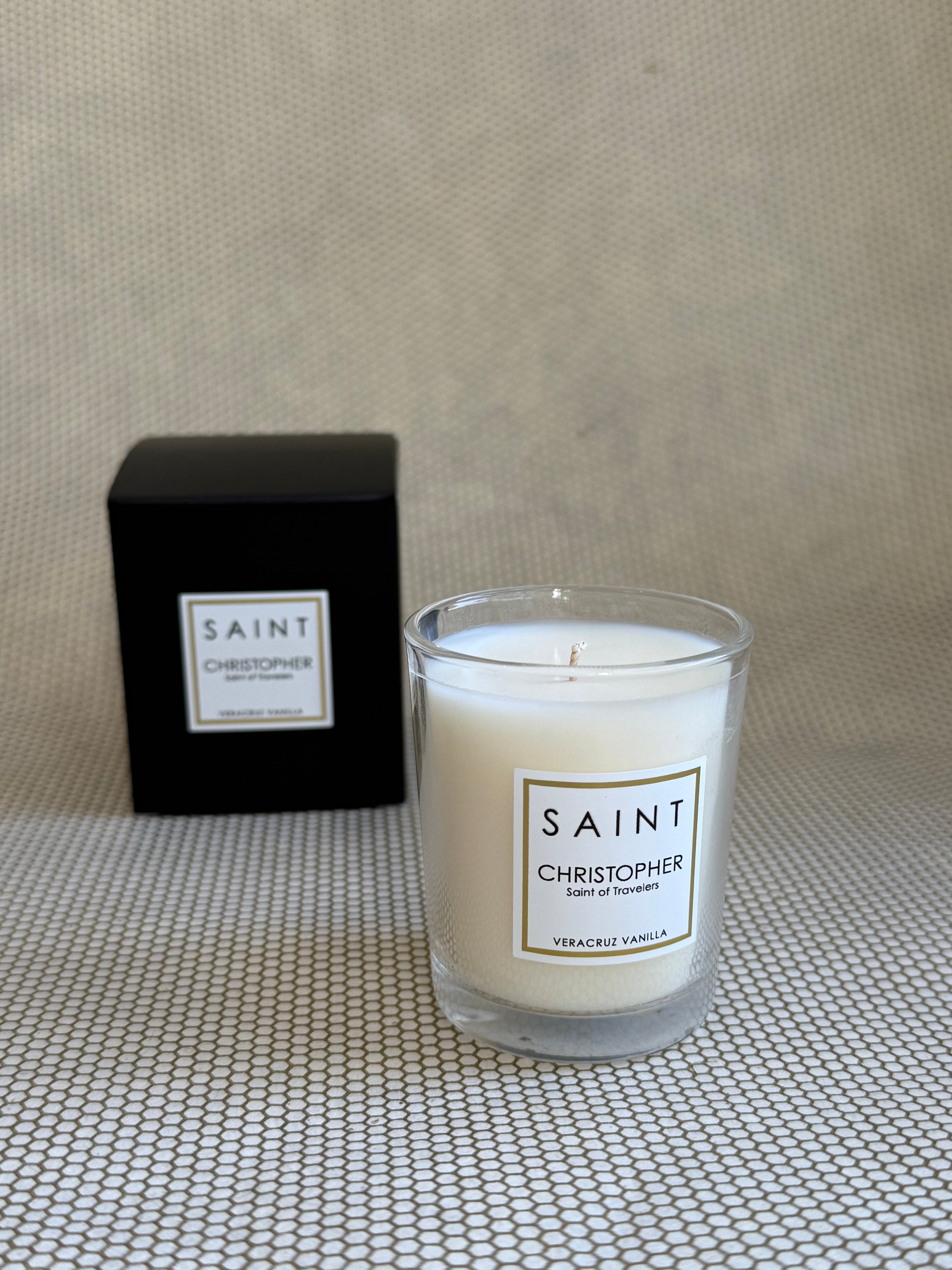 SAINT small votive candle. clear glass white wax in black box. saint christopher vanilla. 3 oz.(2.5 oz. pour). Measures 2.5"Hx2"D.
