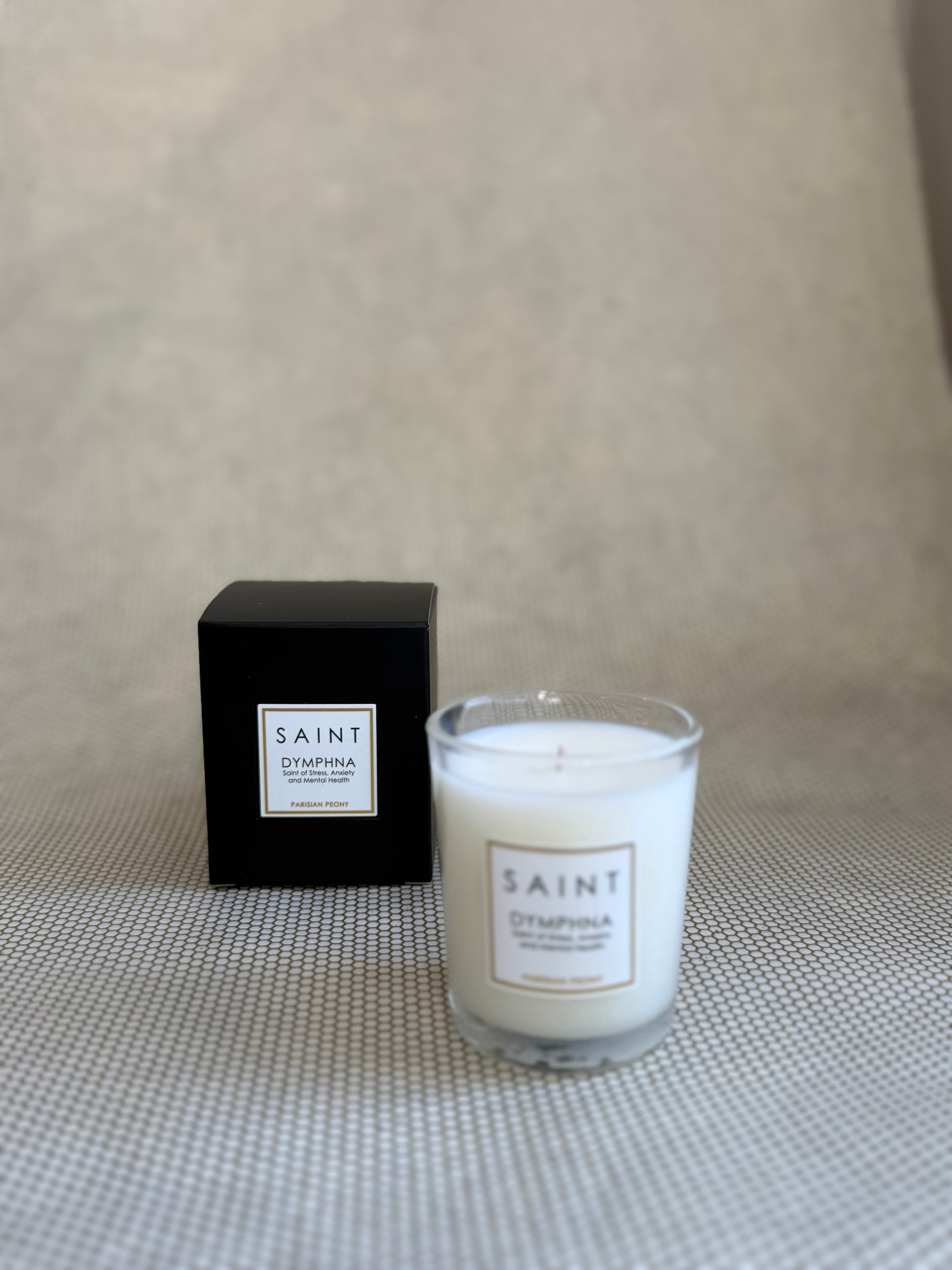 SAINT small votive candle. clear glass white wax in black box. saint dymphna parisian peony. 3 oz.(2.5 oz. pour). Measures 2.5"Hx2"D.