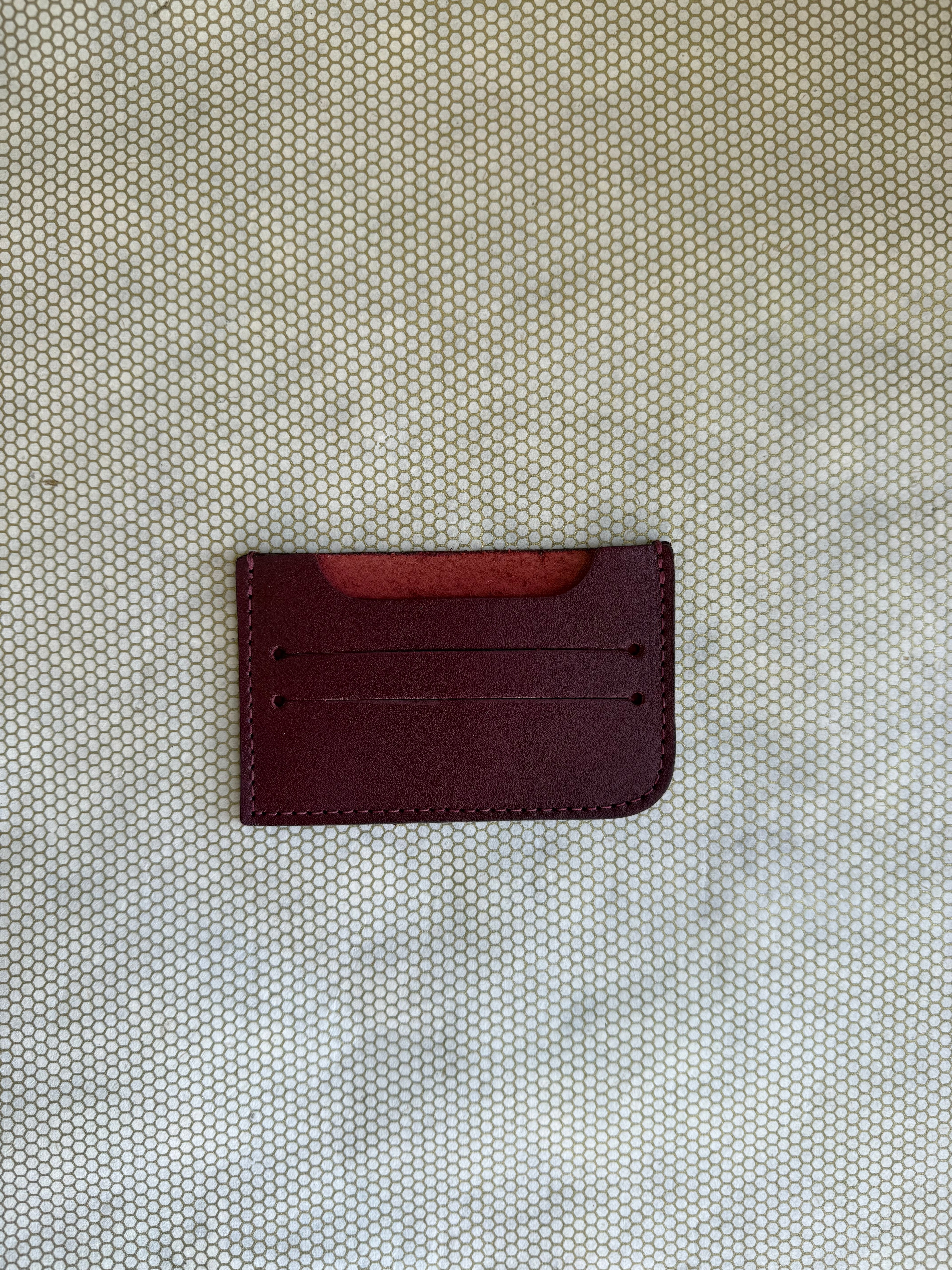 Maroon leather cardholder on a textured beige surface