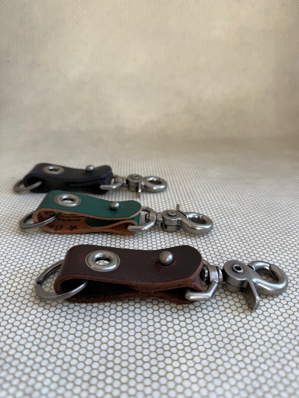 Three leather keychains with metal hooks on a textured surface