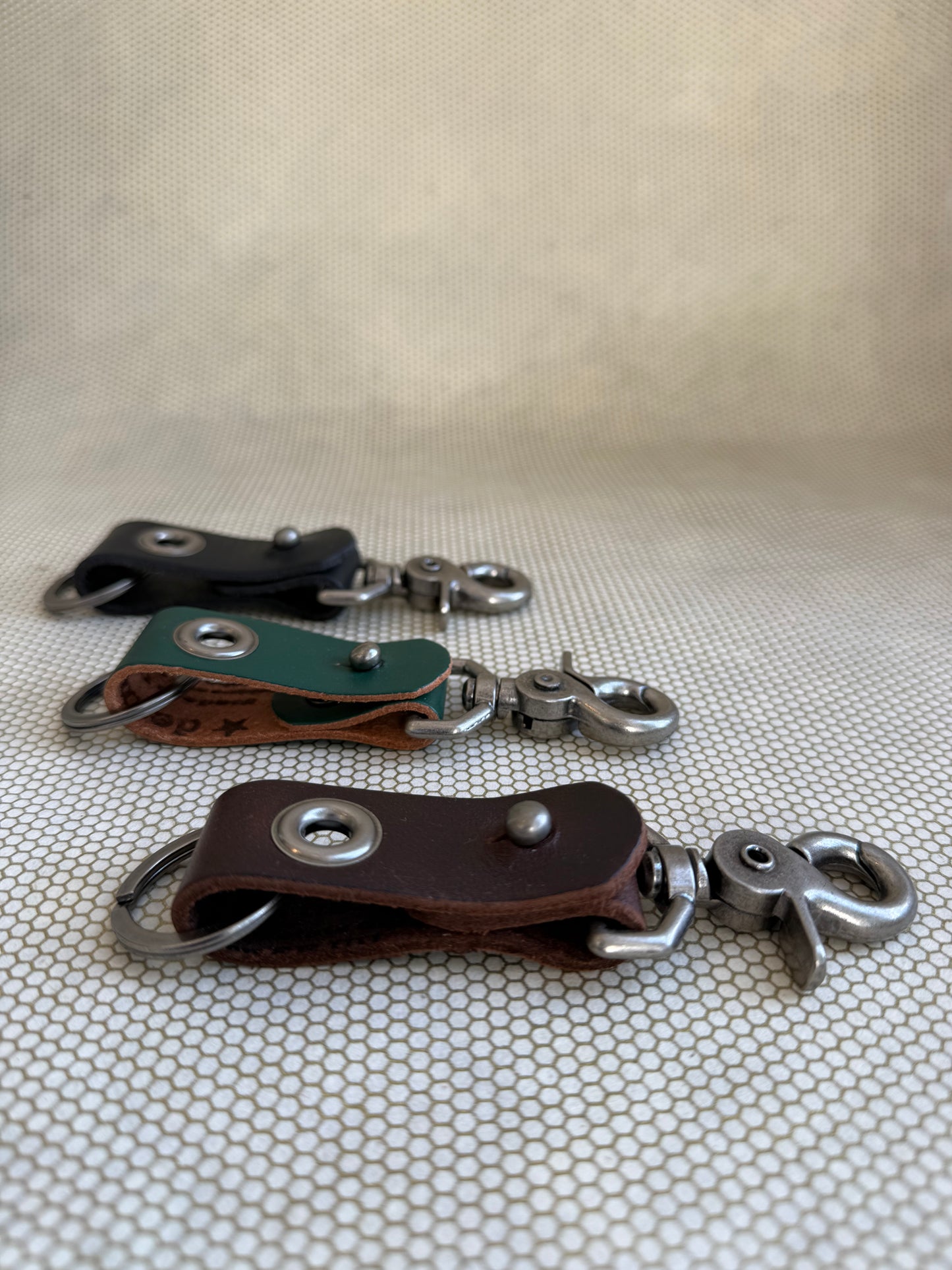 Three leather keychains with metal hooks on a textured surface