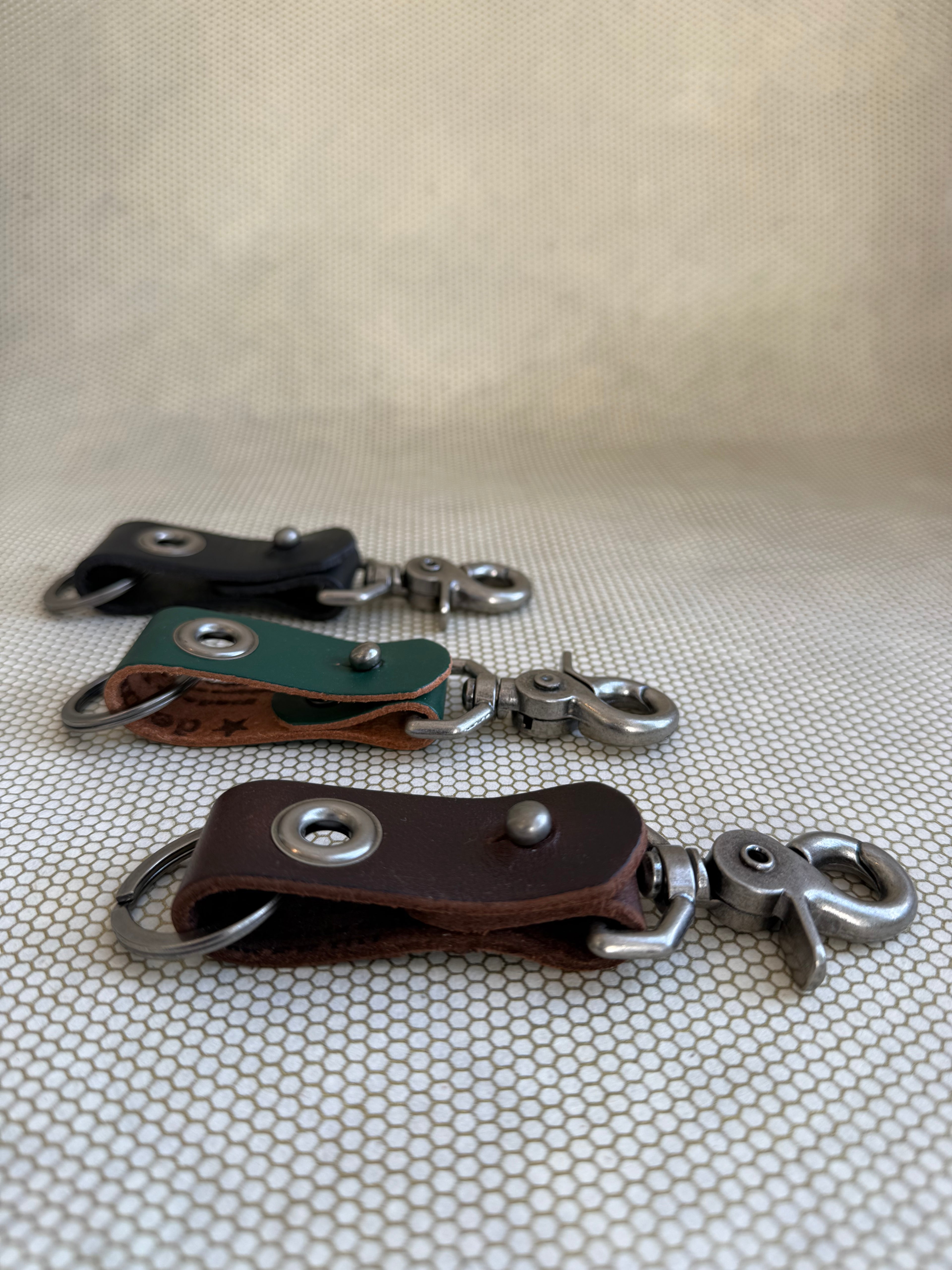 Three leather keychains with metal hooks on a textured surface