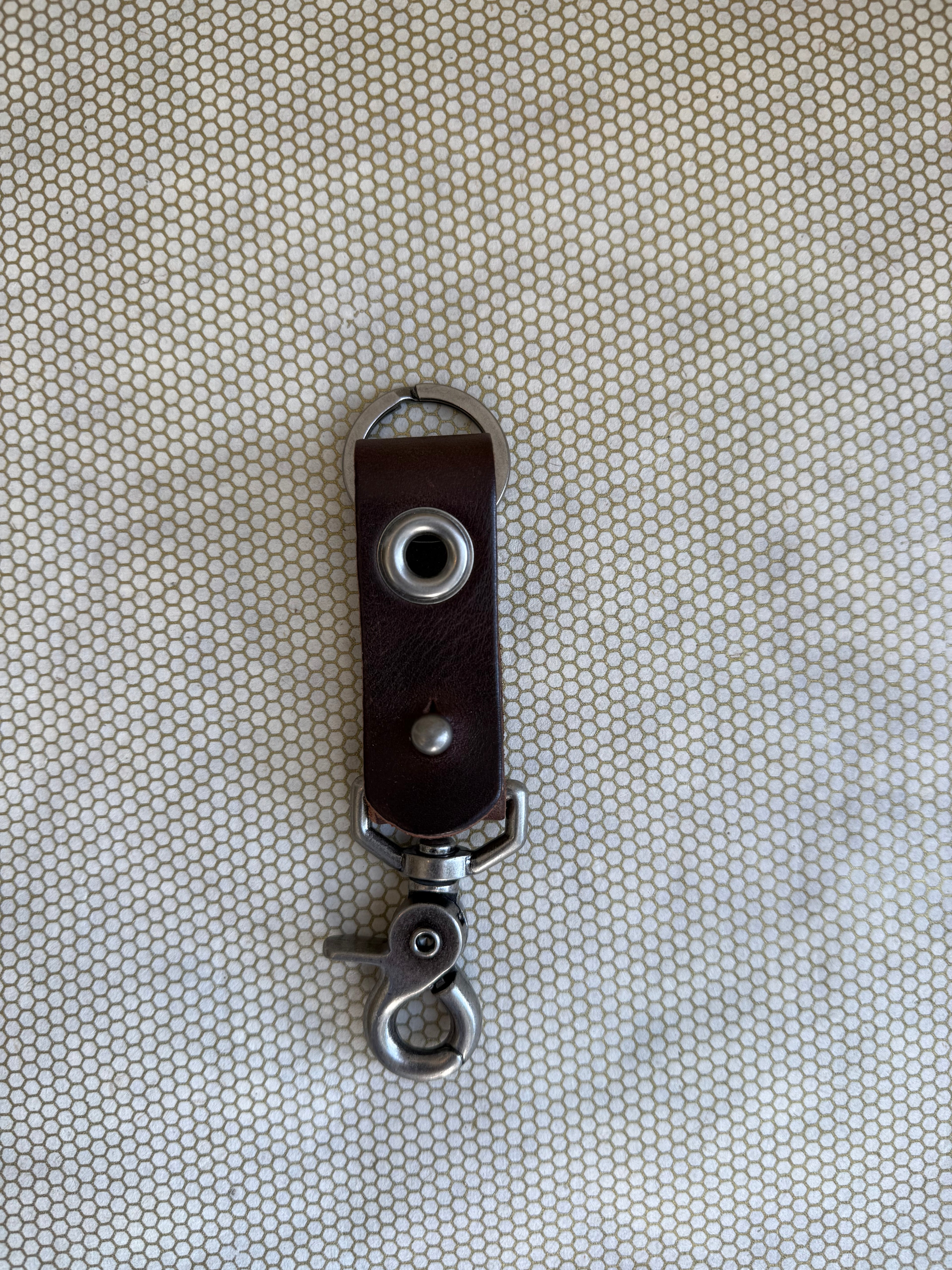 Brown leather key fob with metal clip on a textured beige background