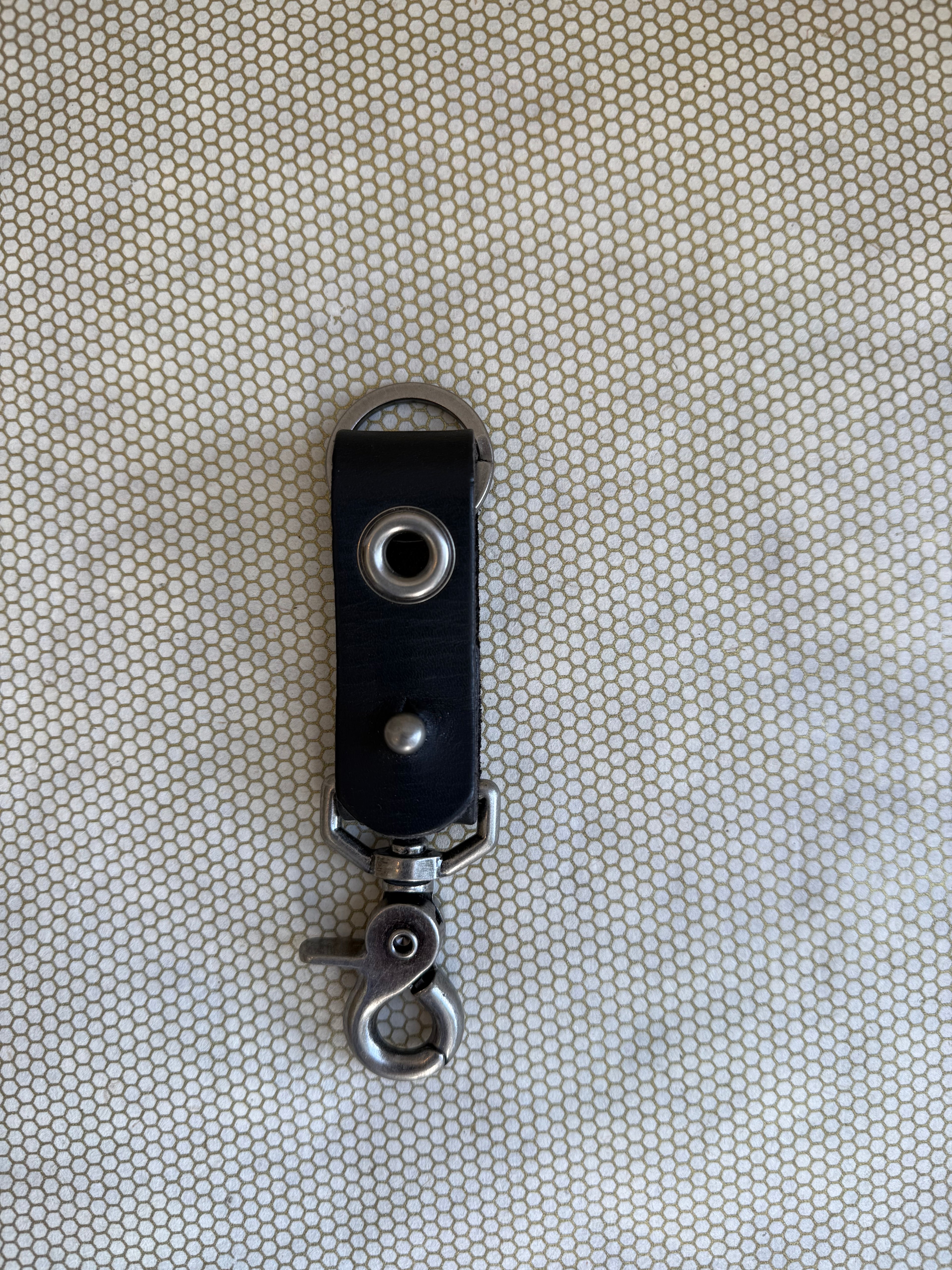 Black leather key fob with metal clip on a textured beige background