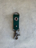 Green leather keychain with metal clasp on a textured beige background