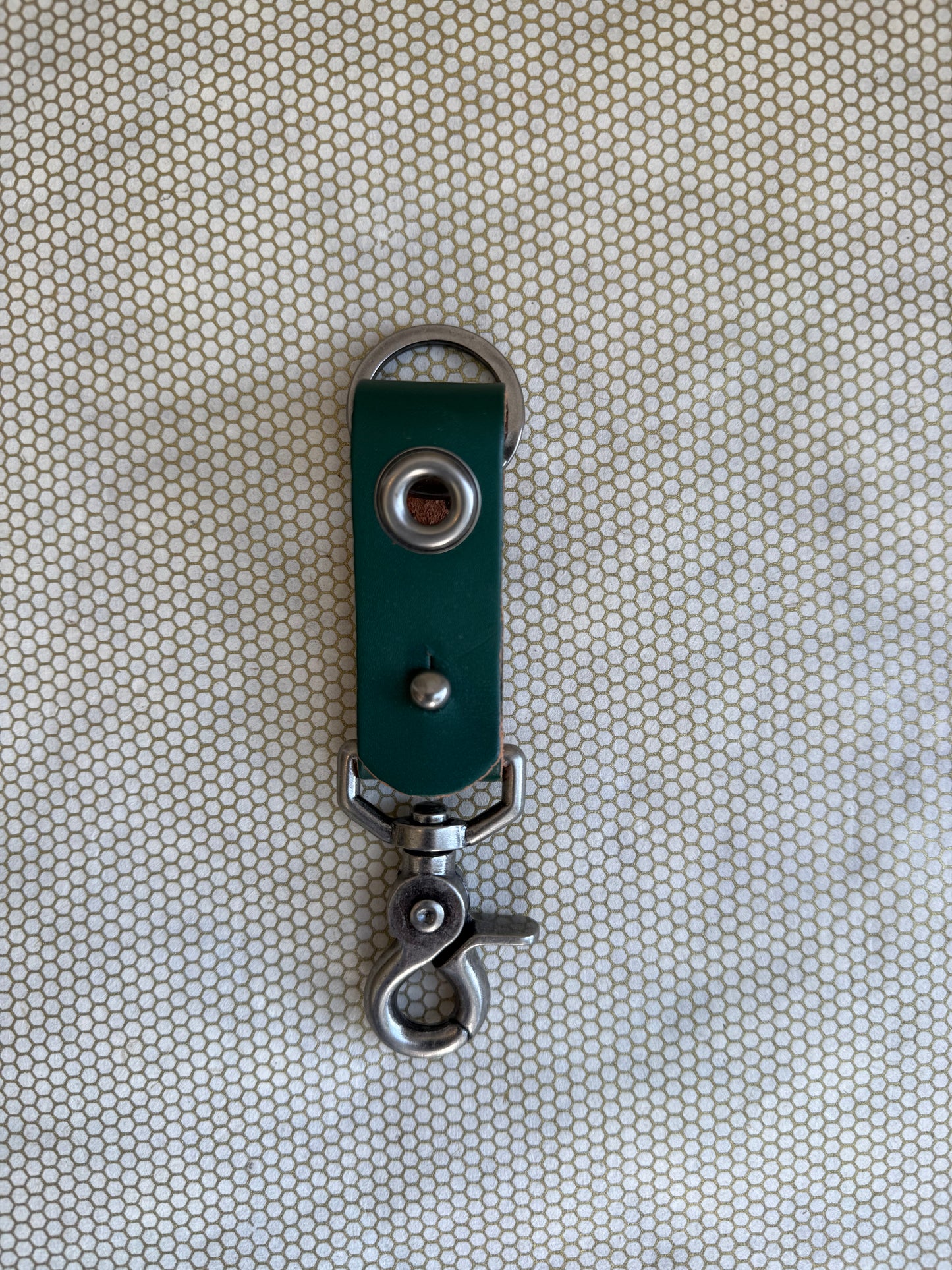 Green leather keychain with metal clasp on a textured beige background