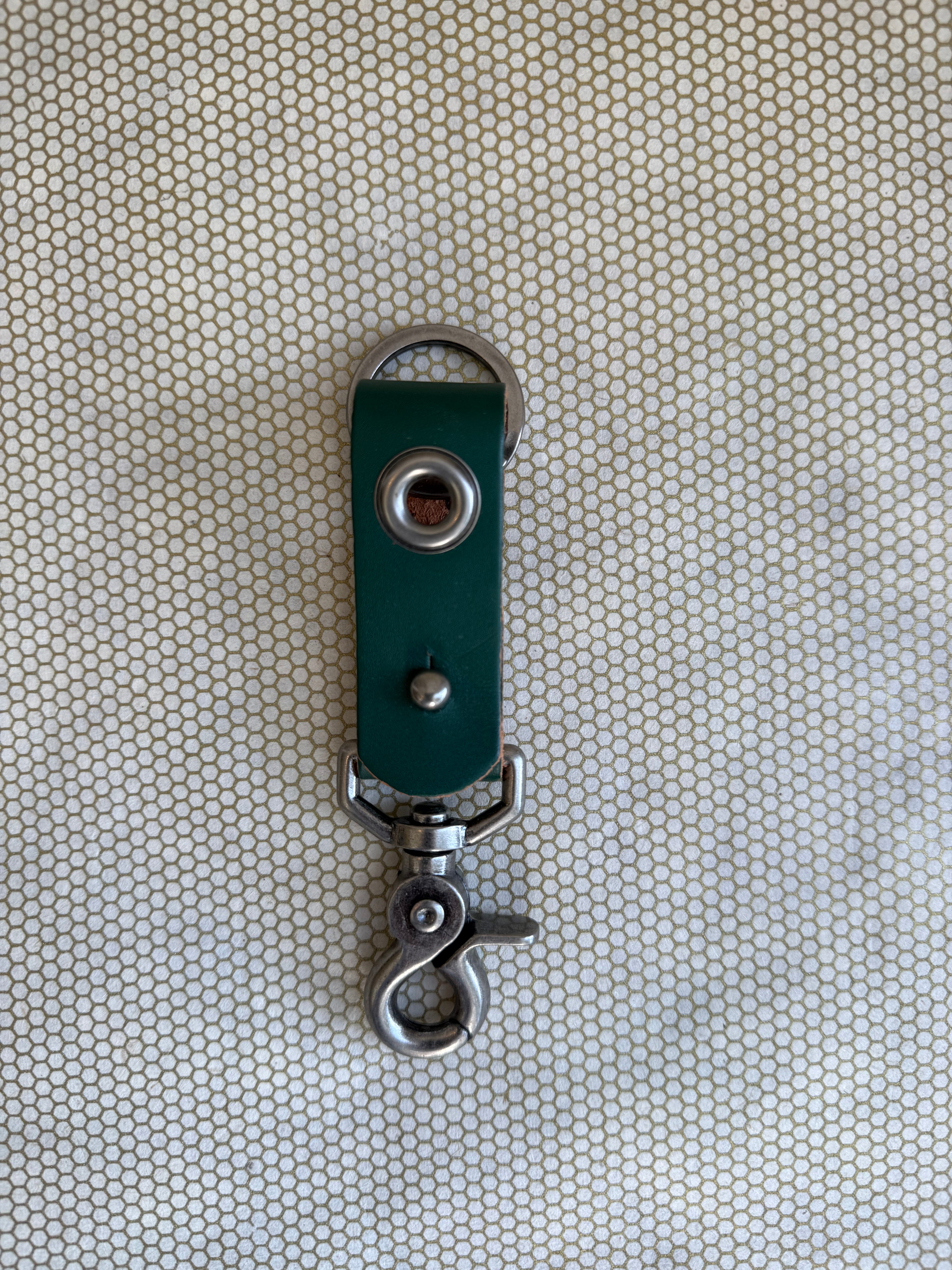 Green leather keychain with metal clasp on a textured beige background