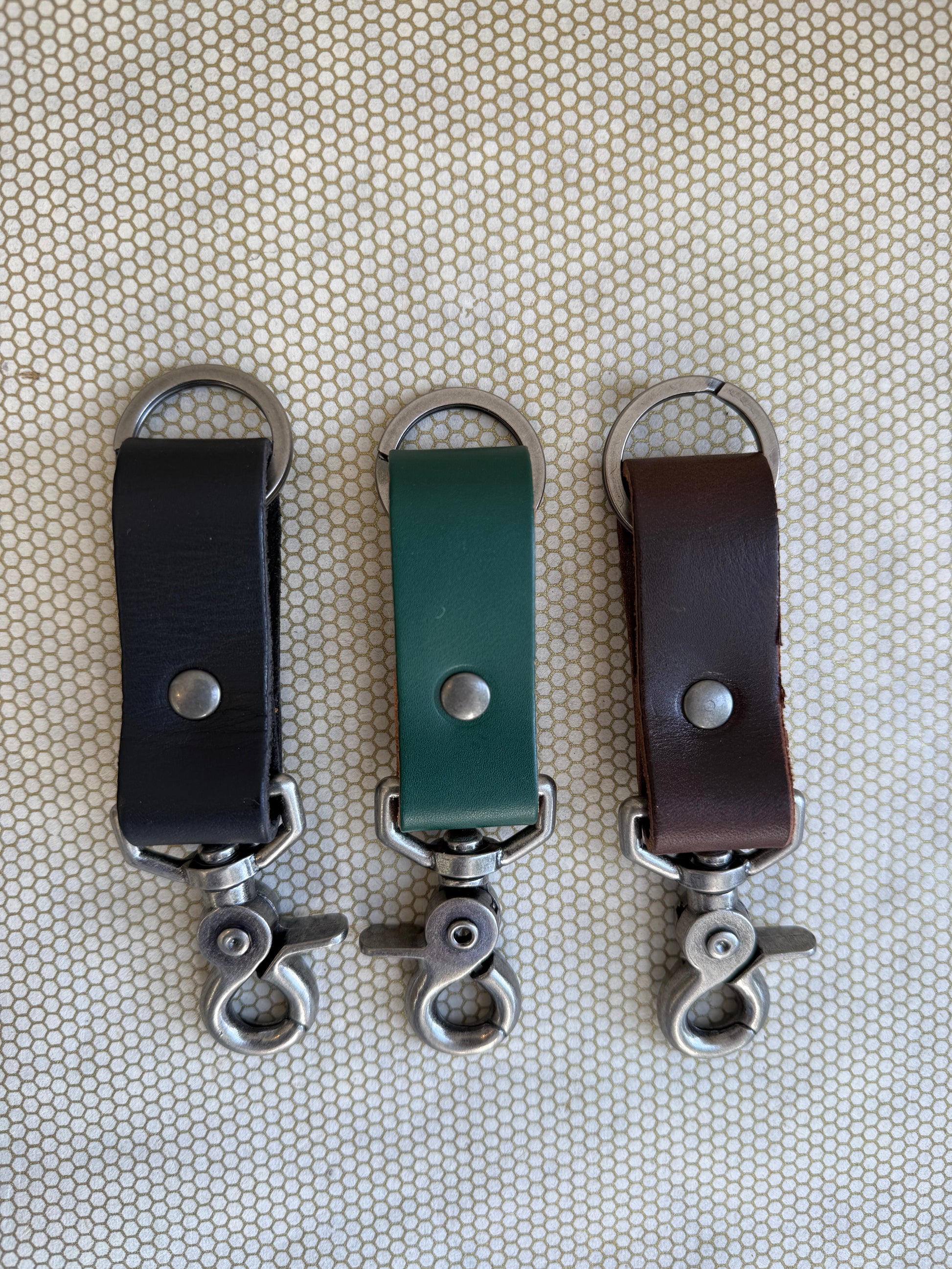 Three leather keychains with metal hooks on a textured beige background