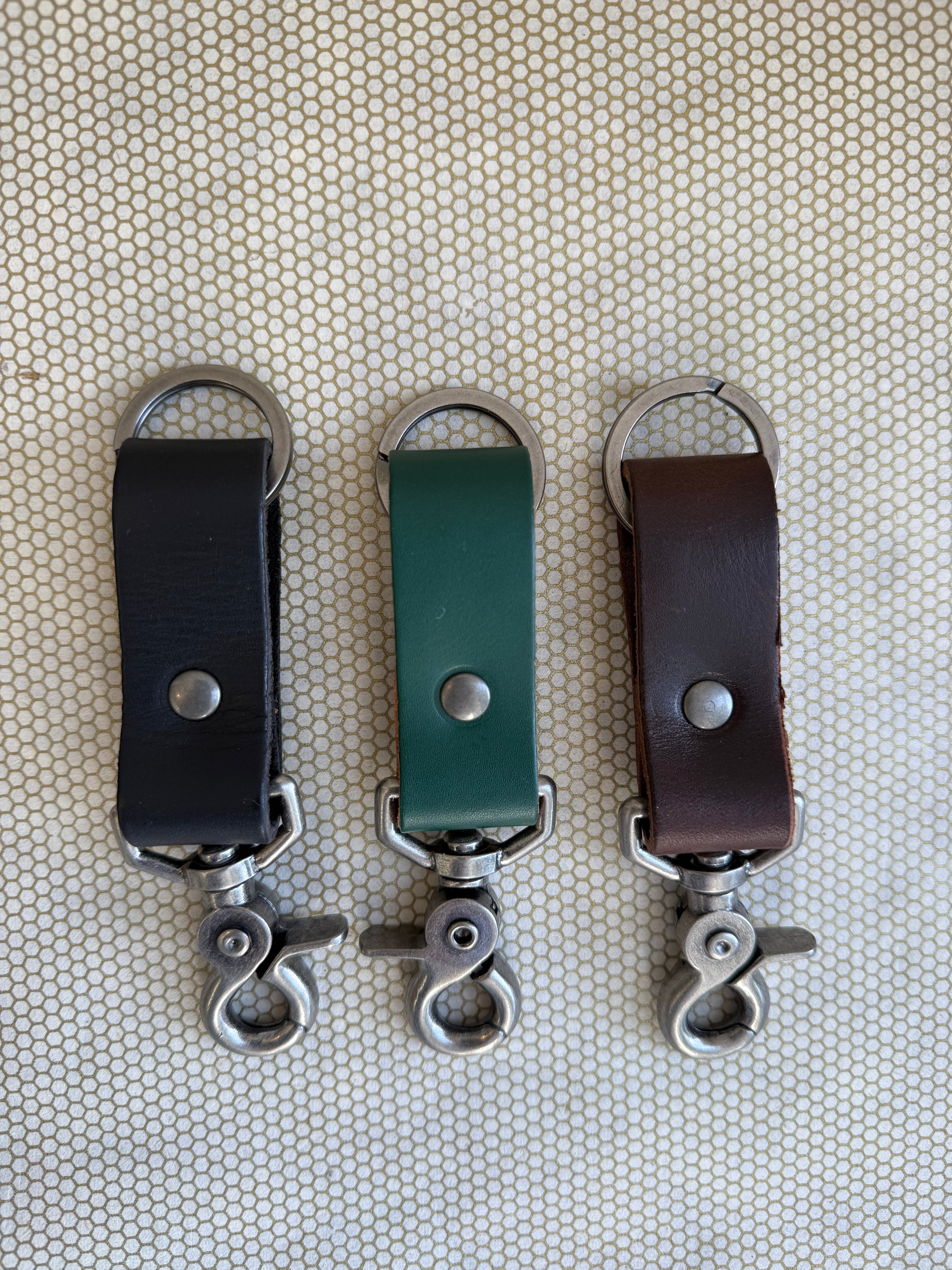Three leather keychains with metal hooks on a textured beige background