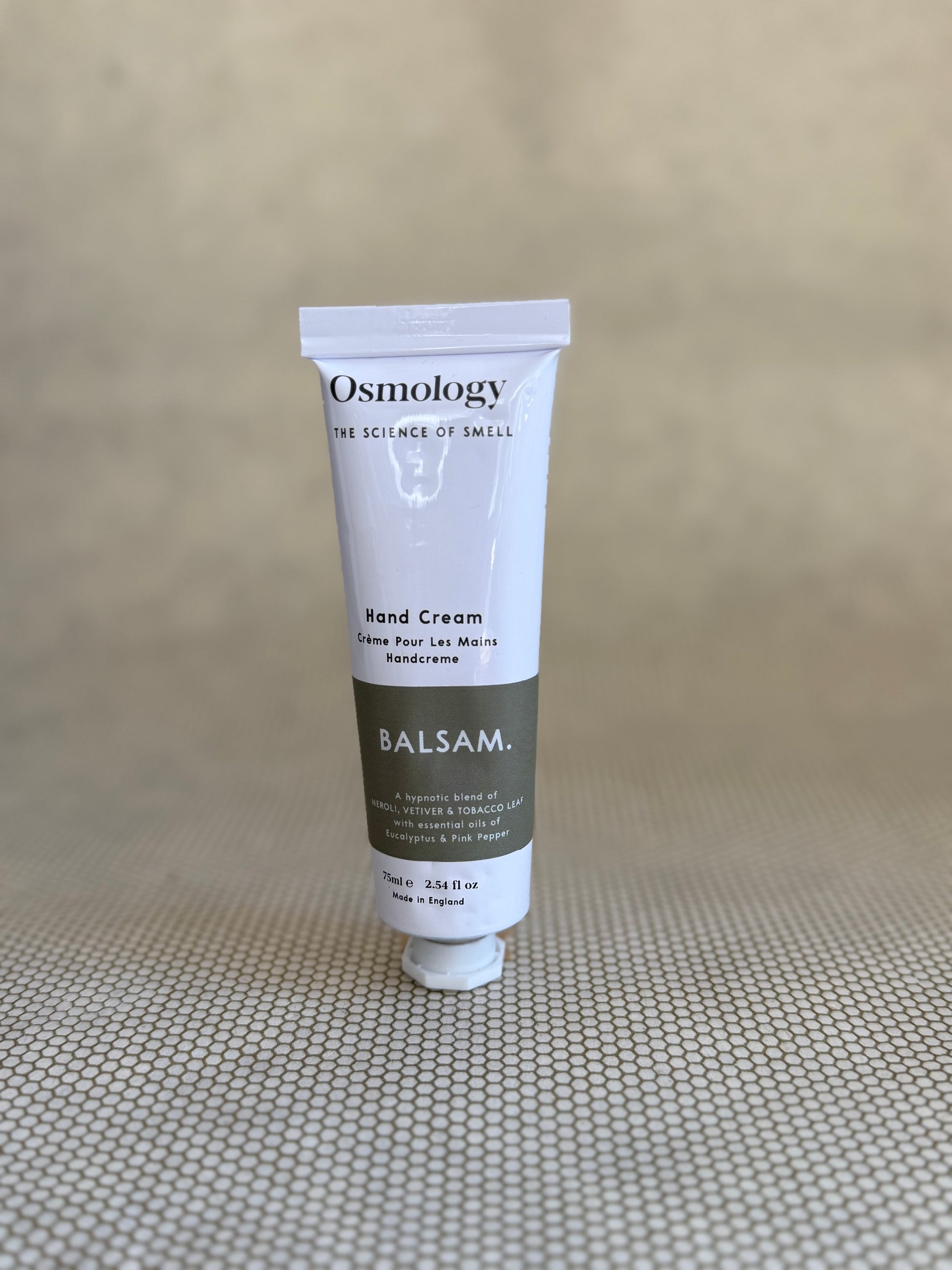Osmology Balsam hand cream tube on a textured beige surface
