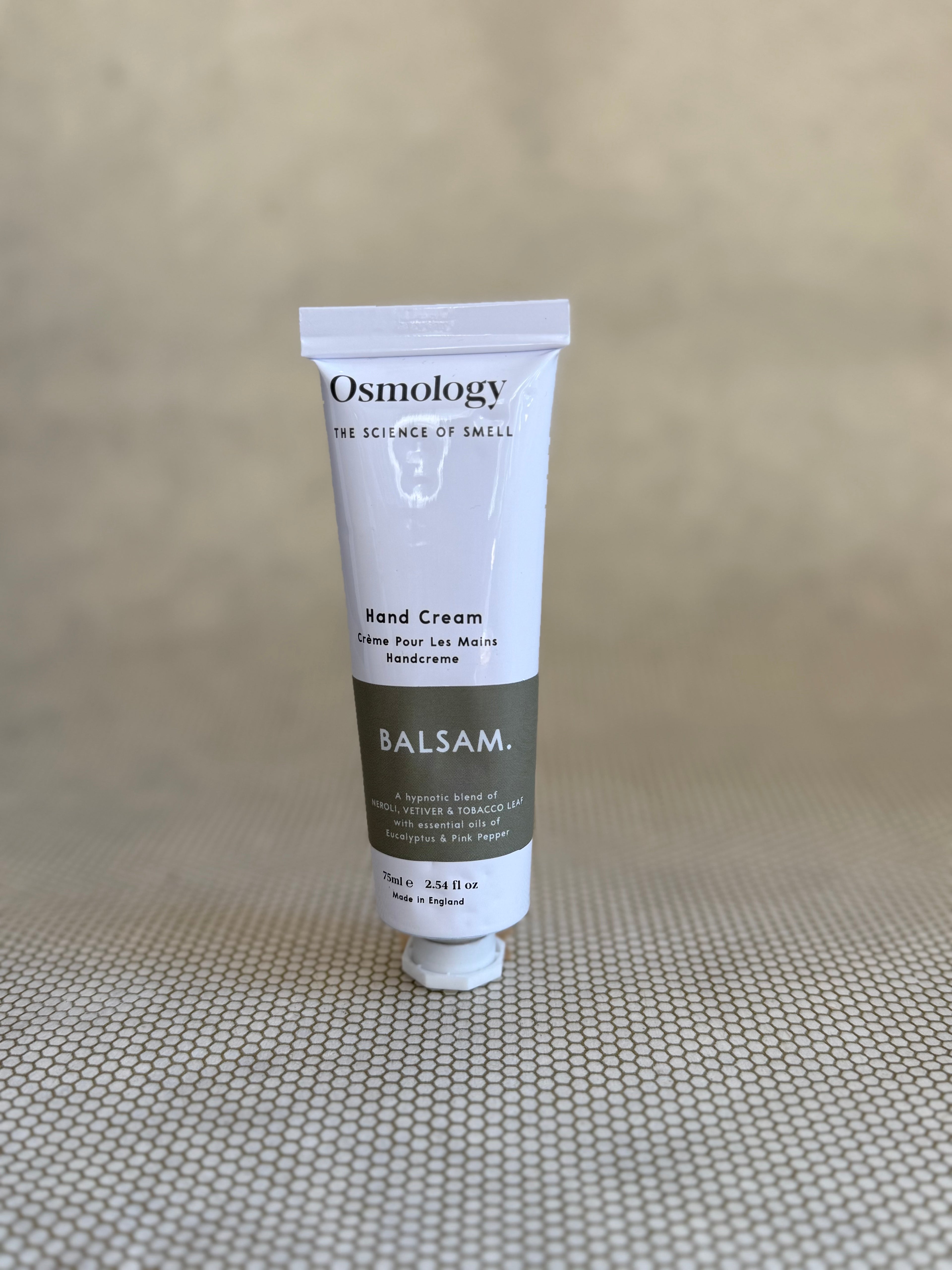 Osmology Balsam hand cream tube on a textured beige surface