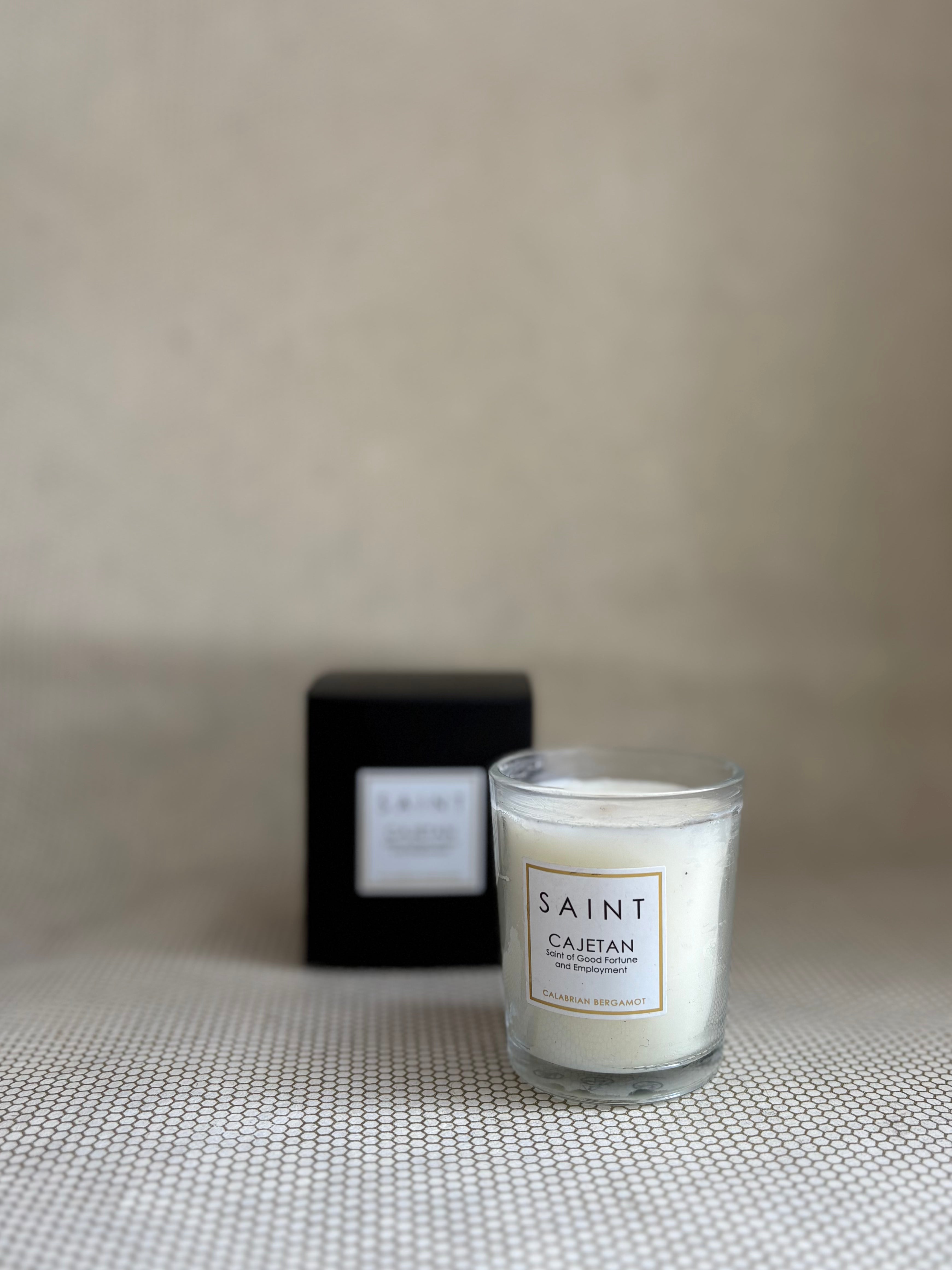 SAINT small votive candle. clear glass white wax in black box. saint cajetan bergamont. 3 oz.(2.5 oz. pour). Measures 2.5"Hx2"D.