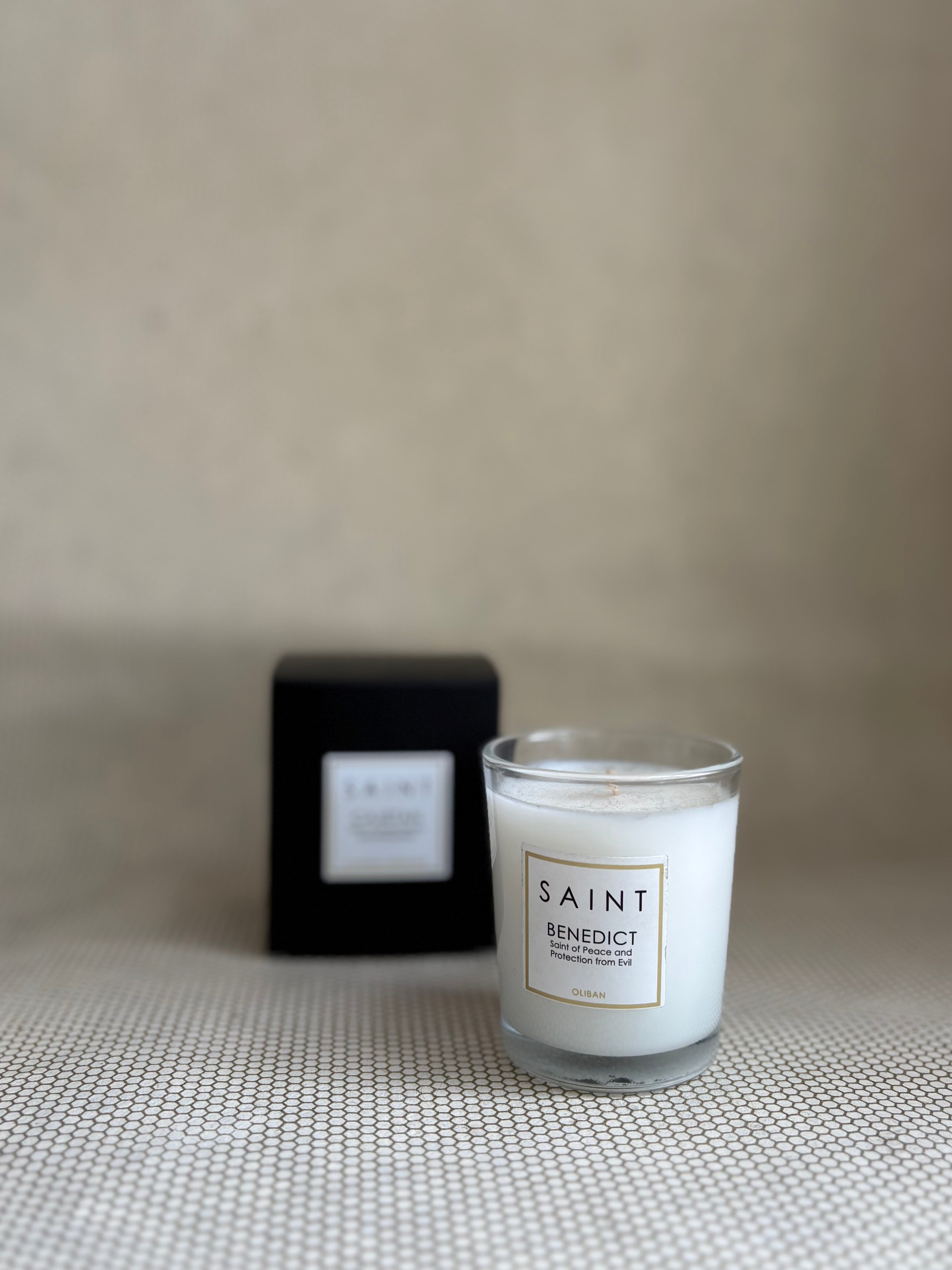 SAINT small votive candle. clear glass white wax in black box. saint benedict oliban. 3 oz.(2.5 oz. pour). Measures 2.5"Hx2"D.