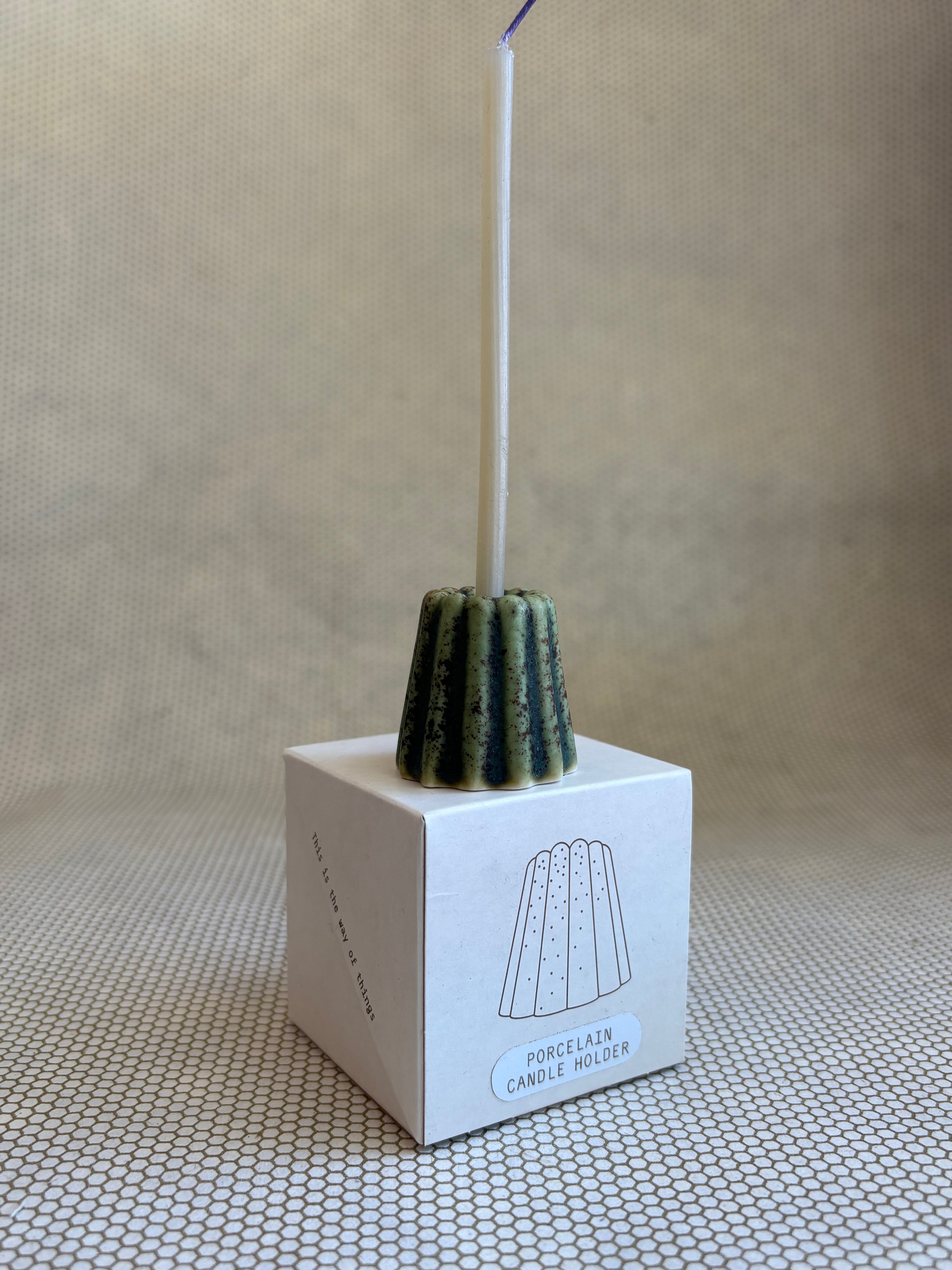candle in small porcelain textured green candle holder on neutral background and small cardboard box.  