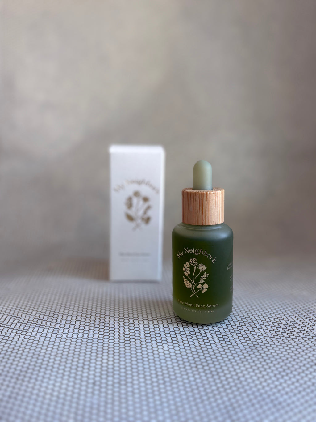 Green dropper bottle of My Neighbor's blue moon face serum and white packaging box in background. 