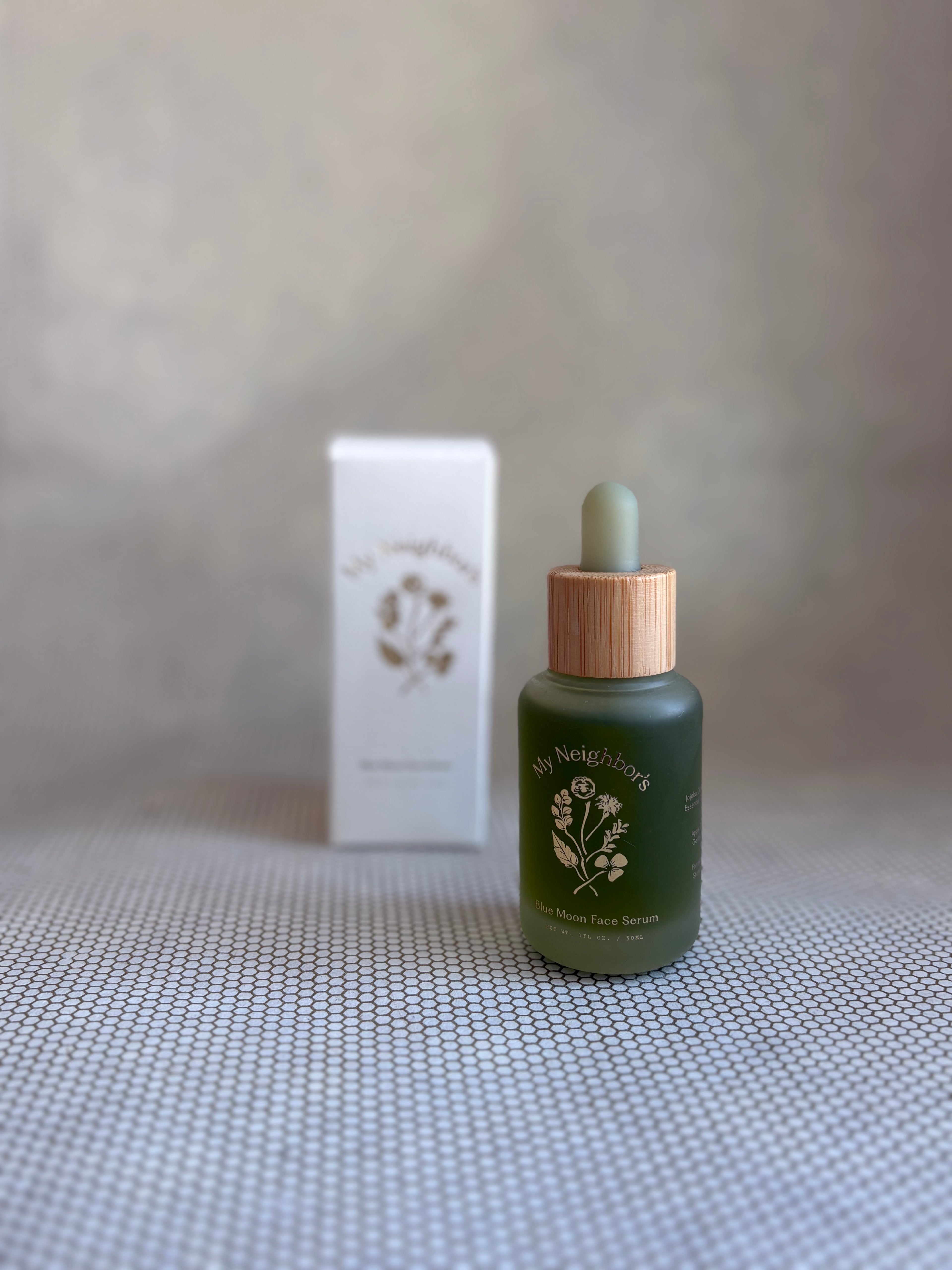 Green dropper bottle of My Neighbor's blue moon face serum and white packaging box in background. 