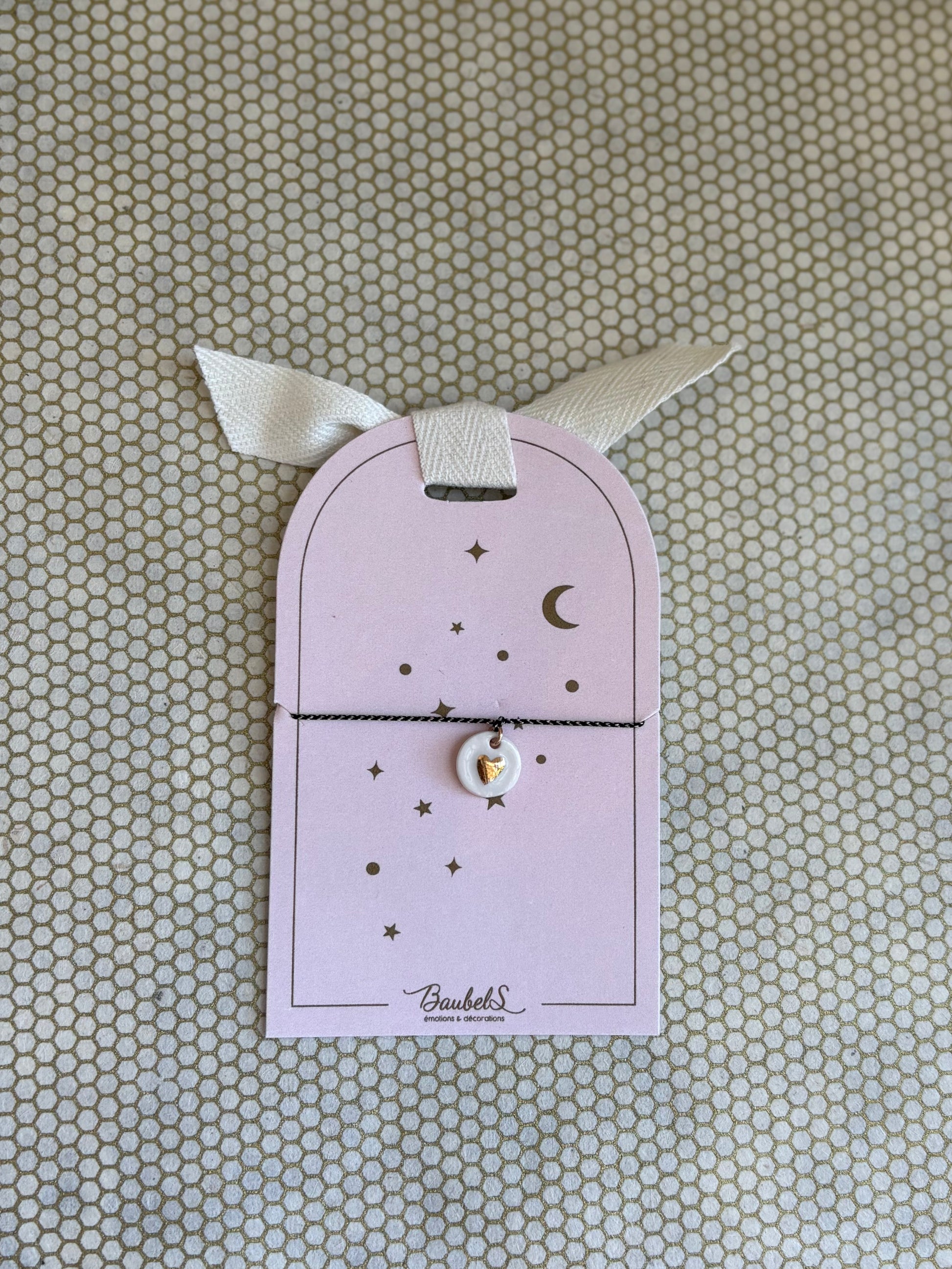 pink cardboard packaging and black string charm bracelet with heart. 