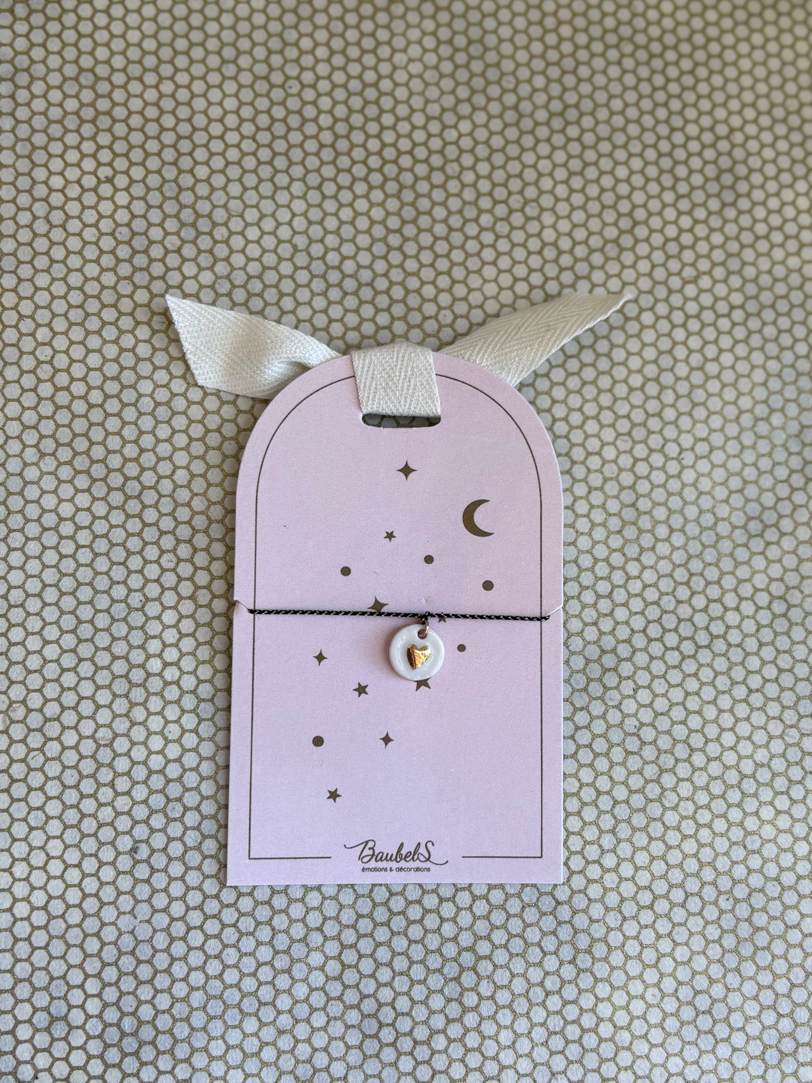 pink cardboard packaging and black string charm bracelet with heart. 