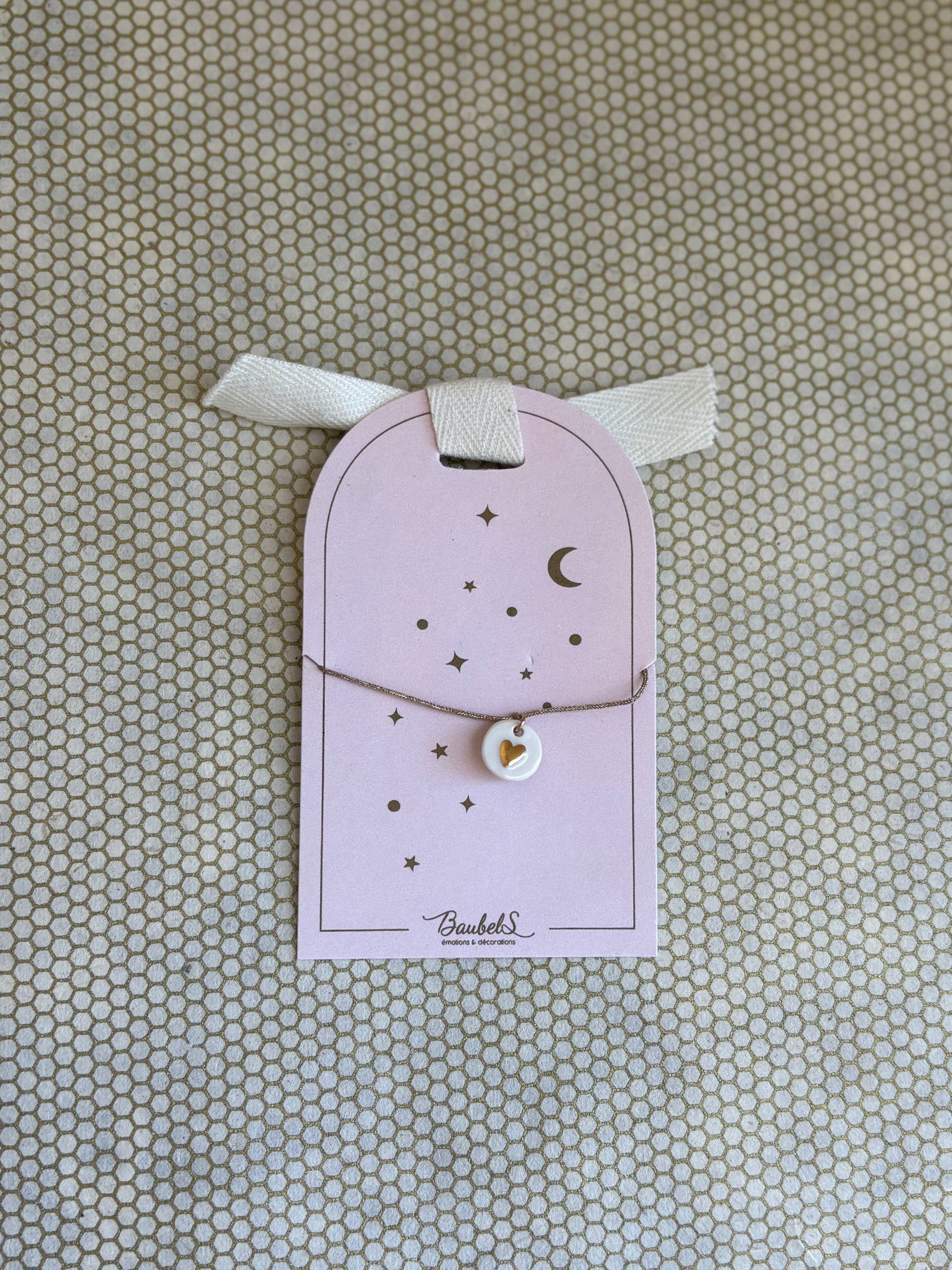 pink cardboard packaging and gold string charm bracelet with heart. 