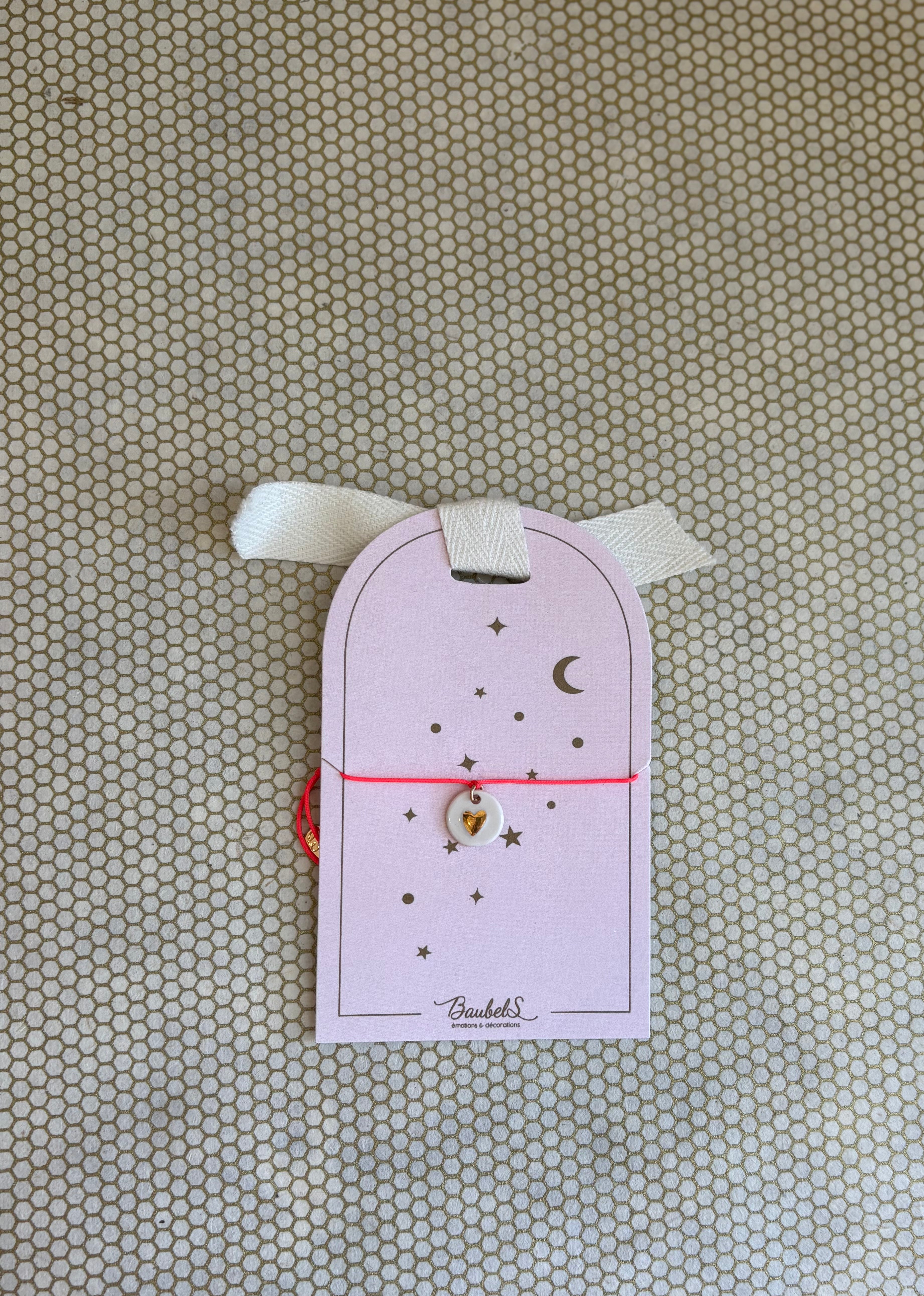 pink cardboard packaging and pink string charm bracelet with heart. 