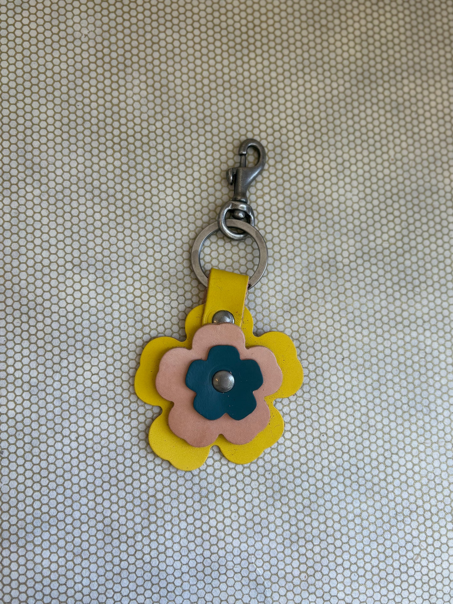 Floral-shaped keychain with a metal clasp on a textured beige background. yellow, tan, blue. 
