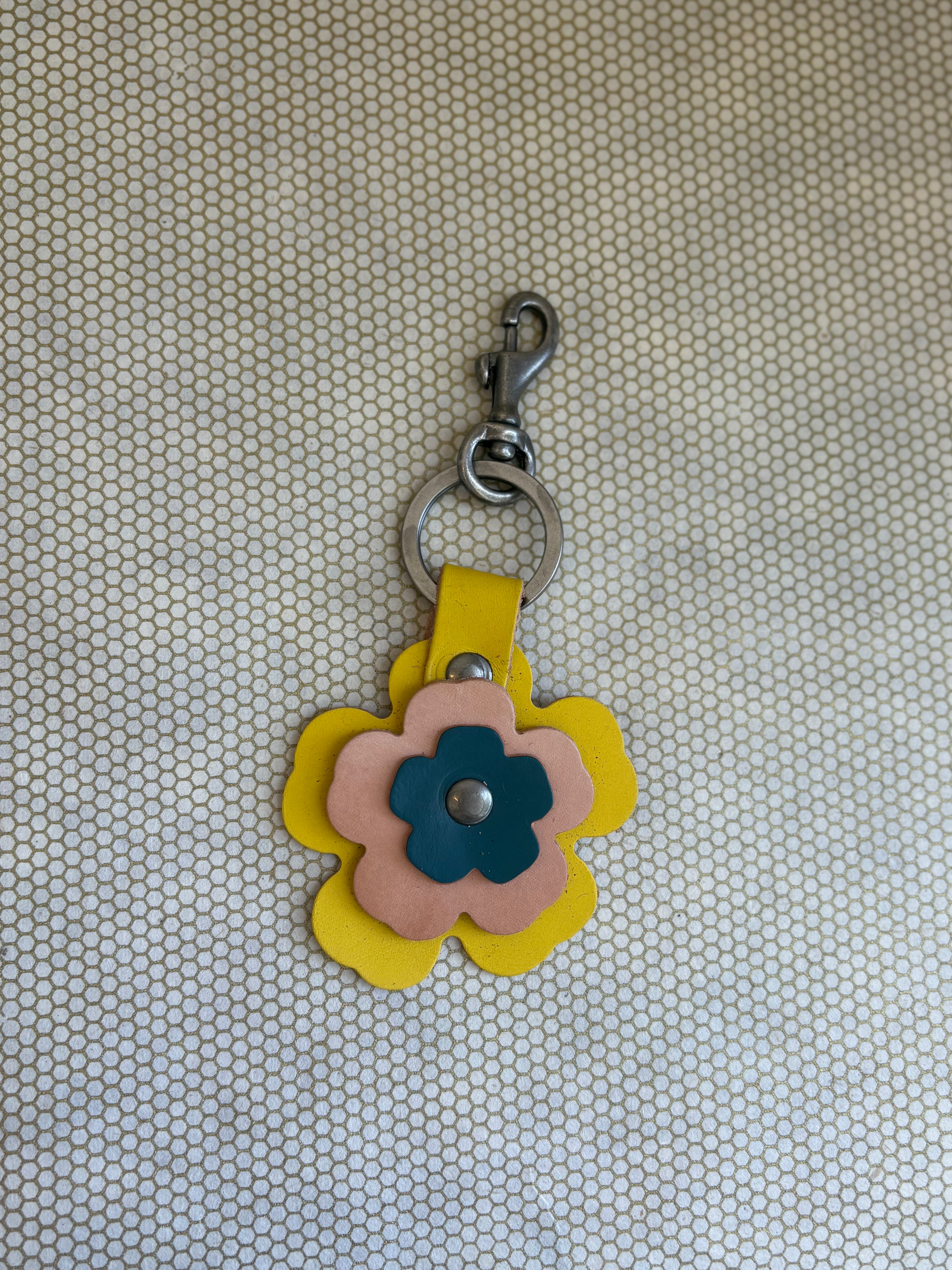 Floral-shaped keychain with a metal clasp on a textured beige background. yellow, tan, blue. 