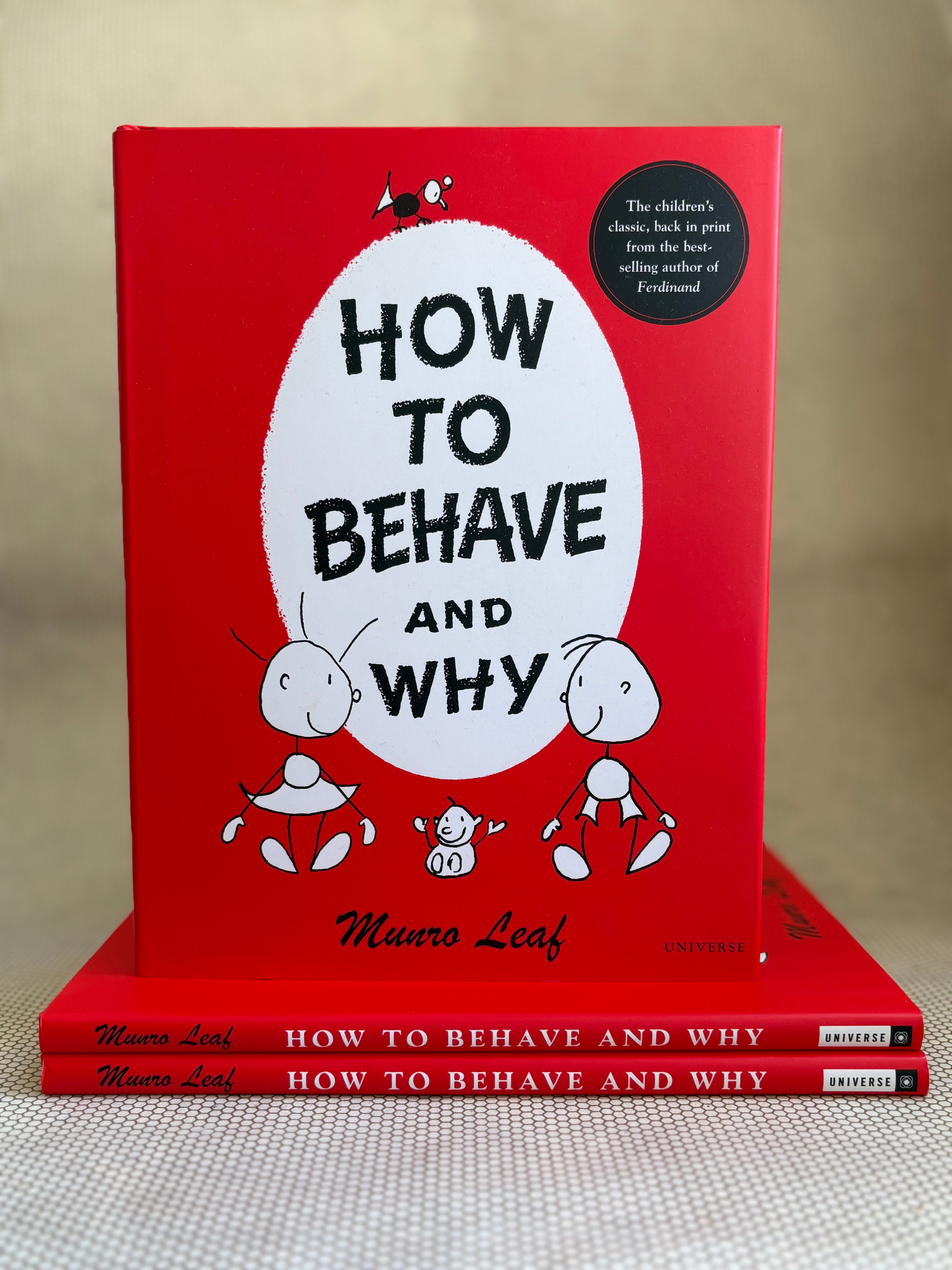 Red book titled 'How to Behave and Why' by Munro Leaf on a beige surface.