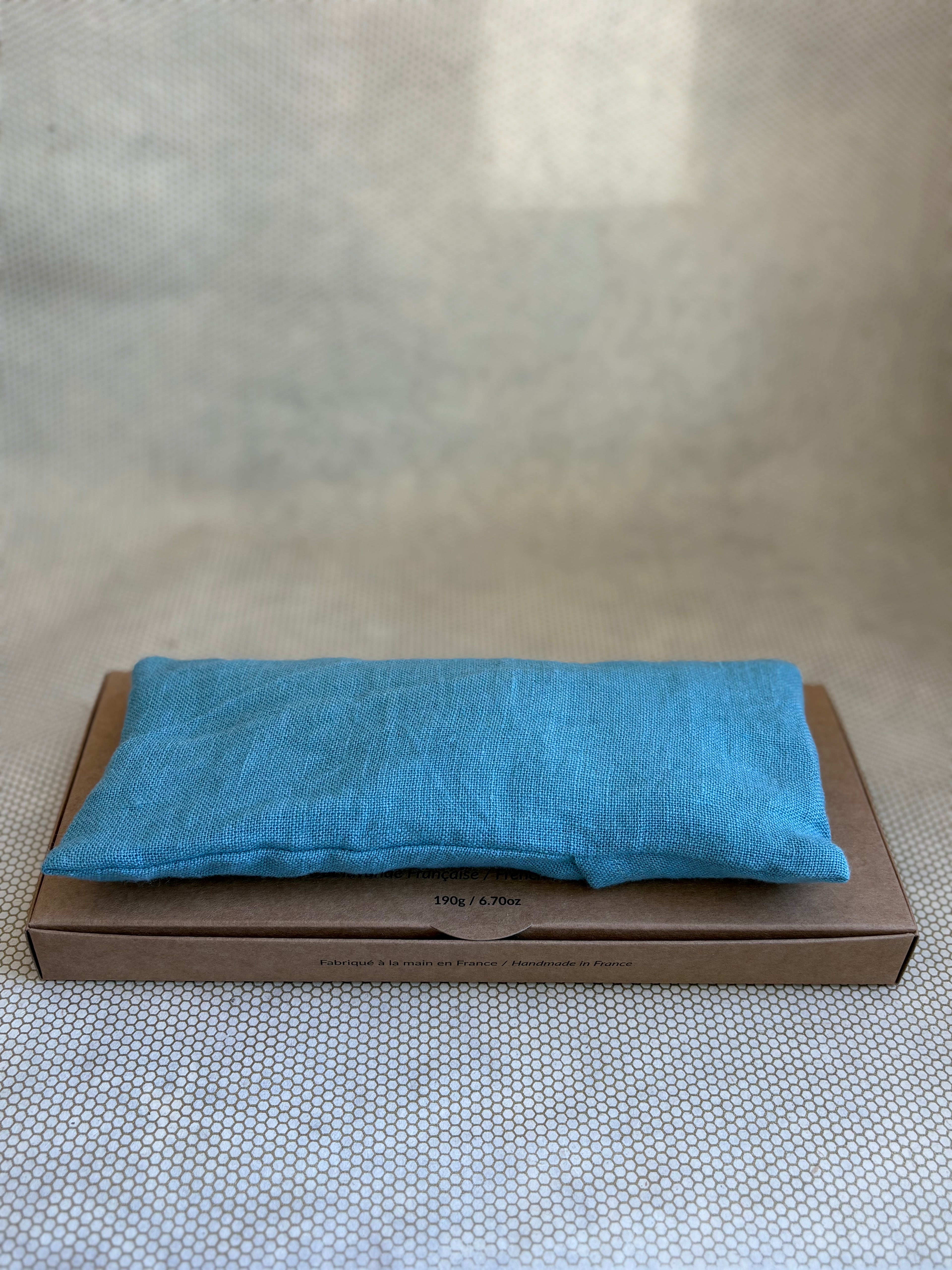 Blue eye pillow on a brown cardboard box with a neutral background