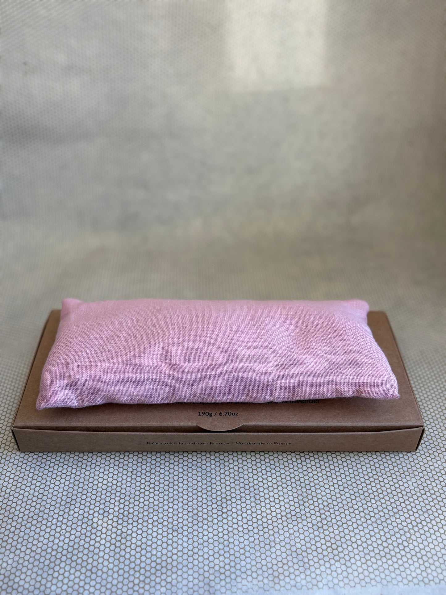 Pink eye pillow on a brown cardboard box against a neutral background
