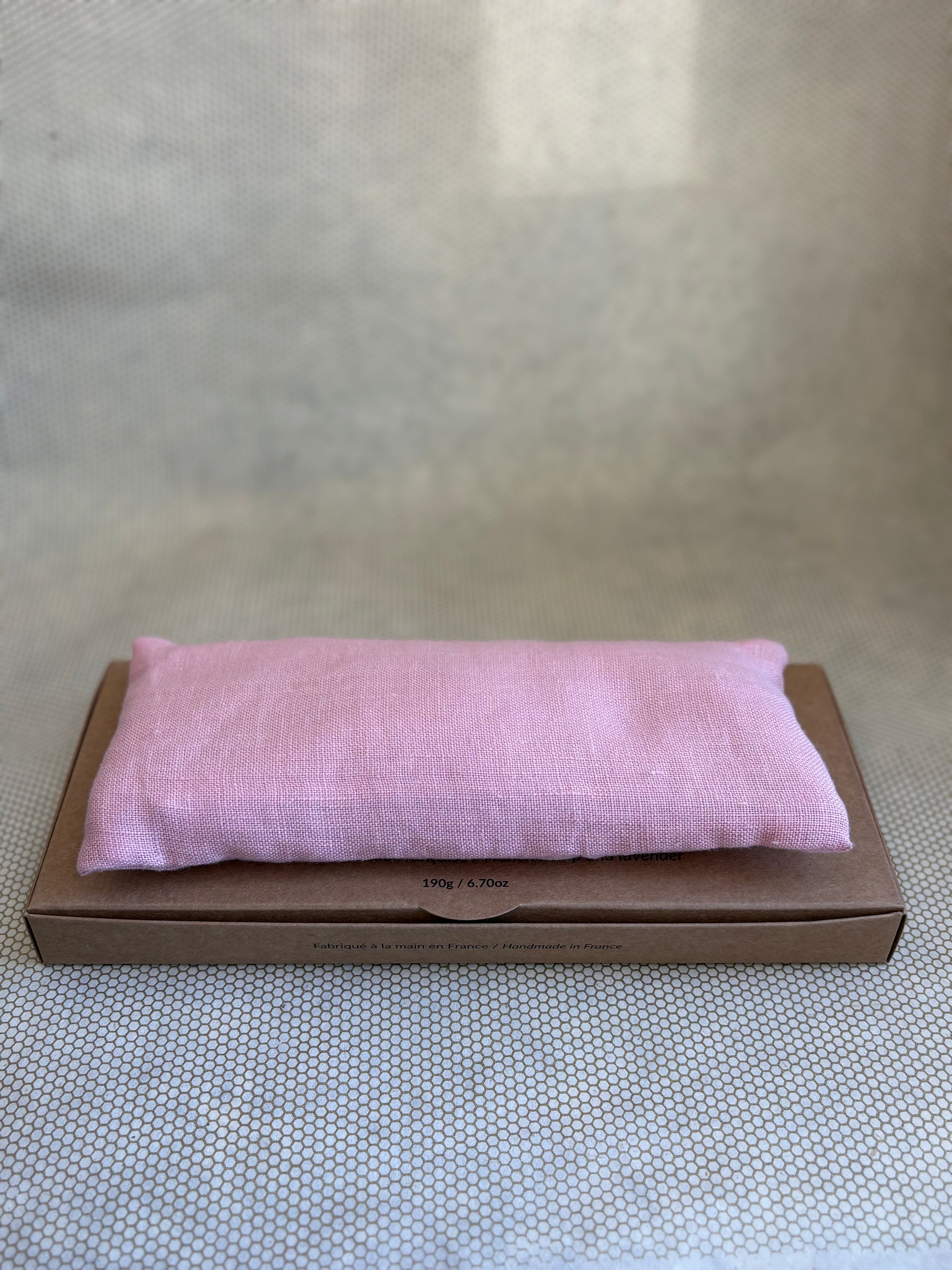 Pink eye pillow on a brown cardboard box against a neutral background