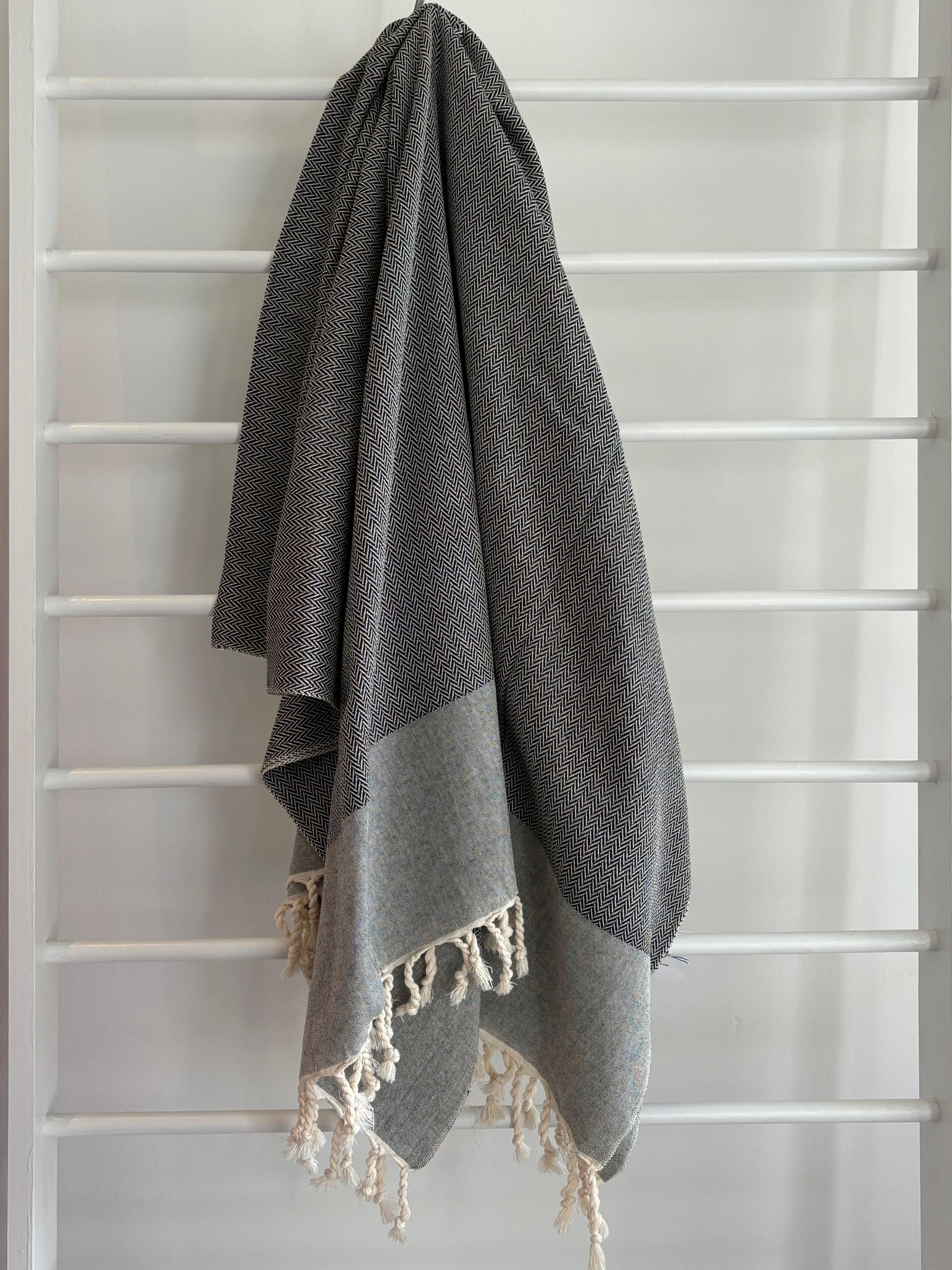 textured black towel with grey trip and white tassels hanging. black textured towel herringbone weave. 