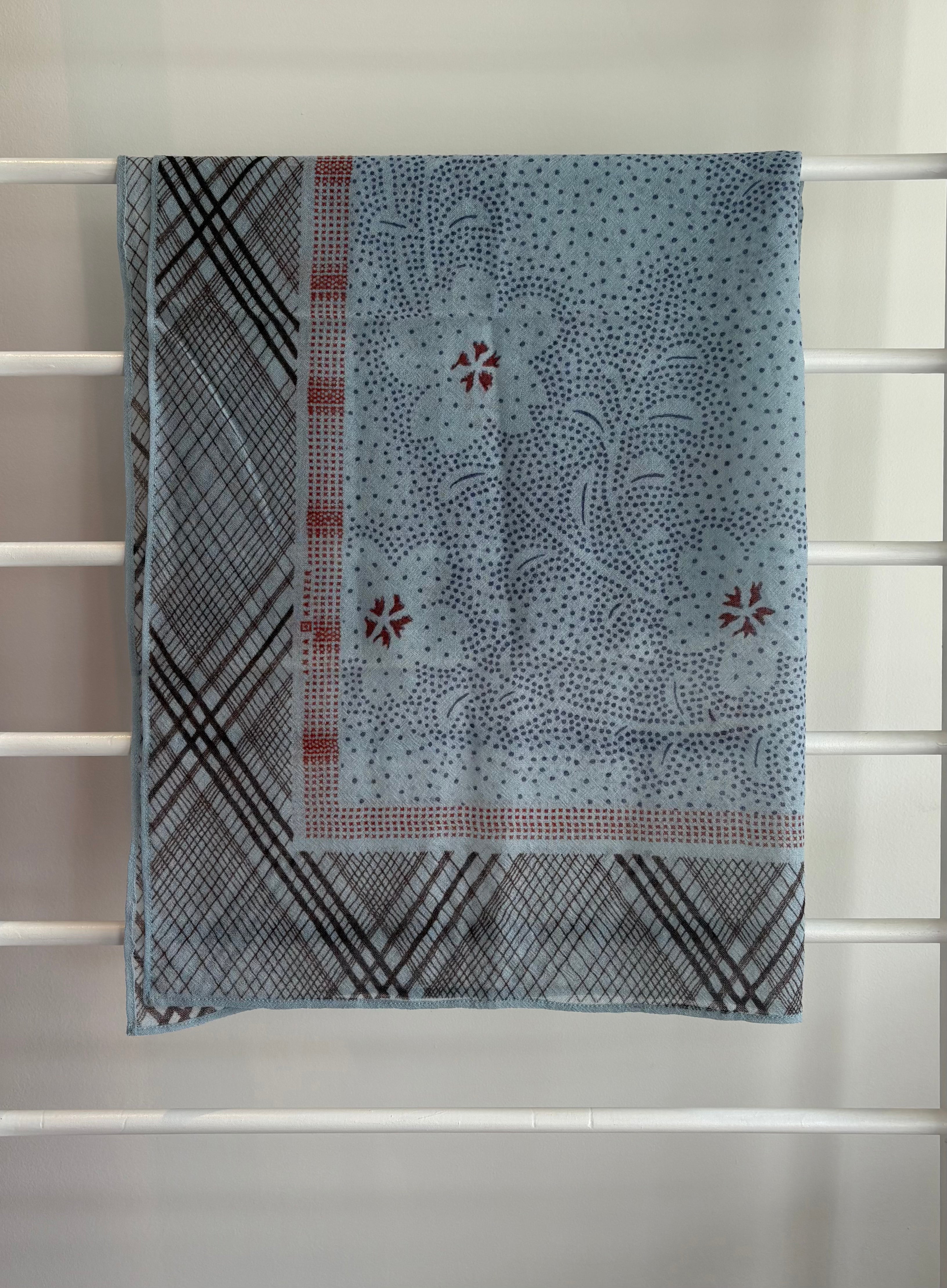 hanging lightweight wool scarf on rack with red, blue and black design.