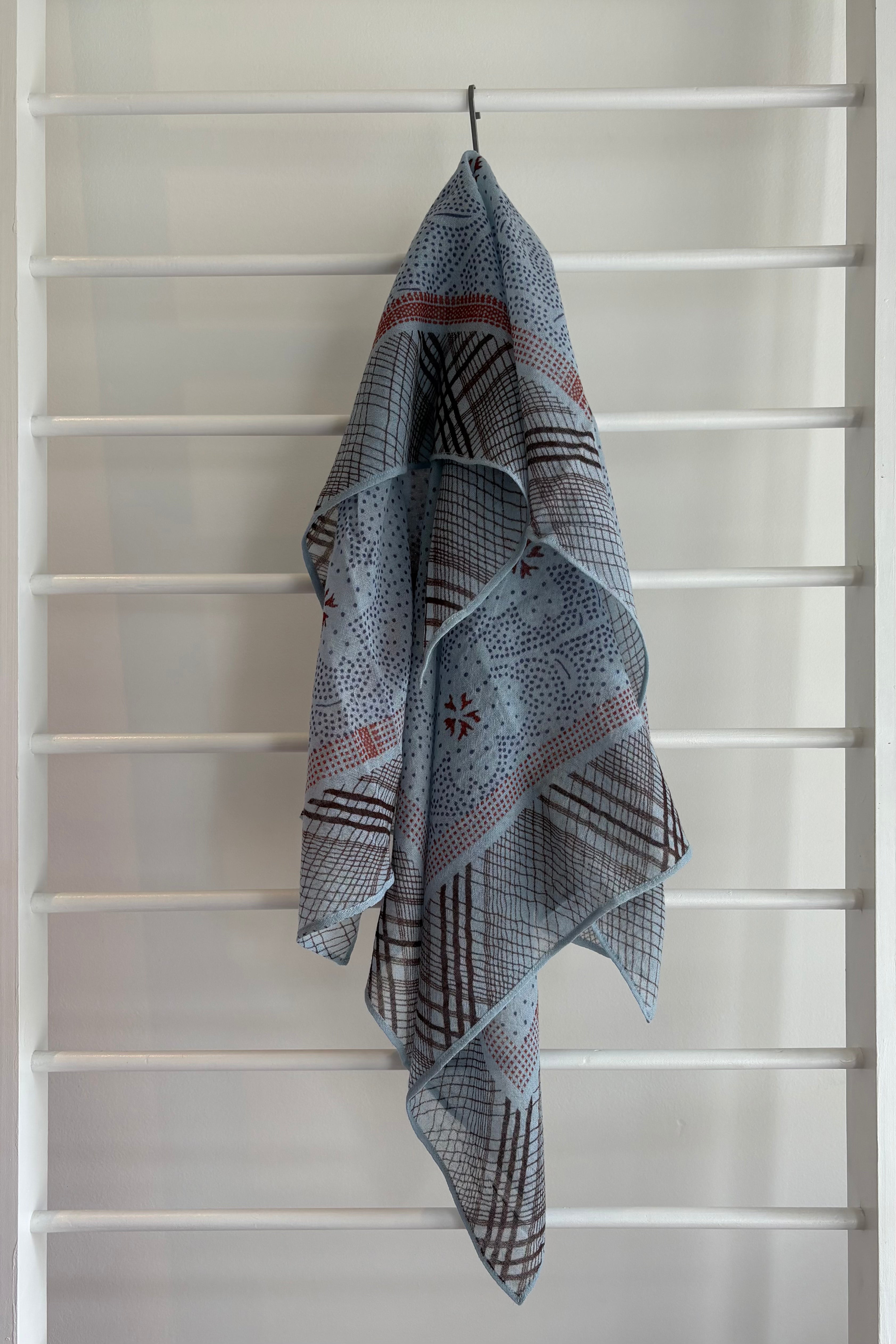 hanging lightweight wool scarf on rack with red, blue and black design.