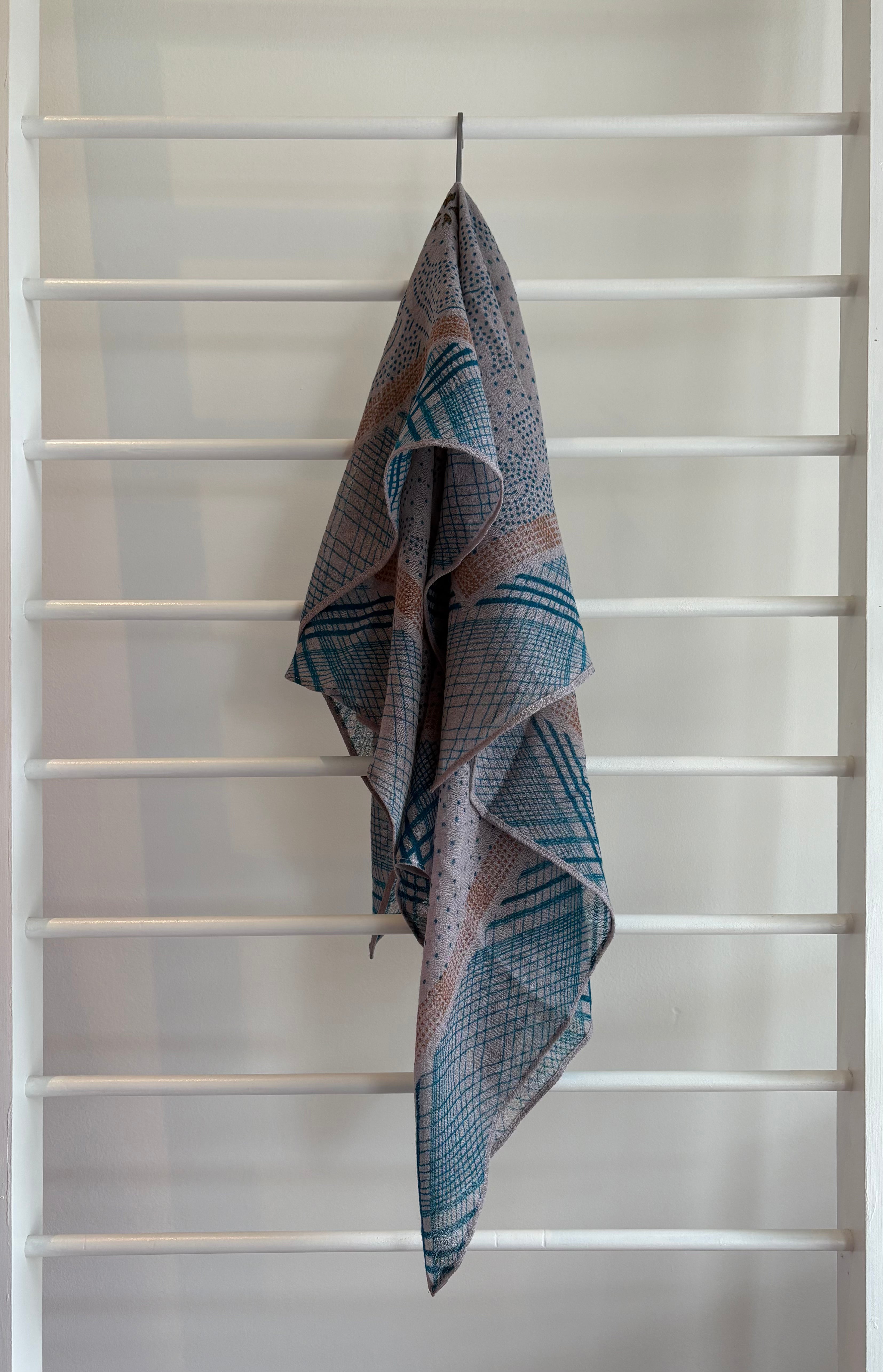 hanging lightweight wool scarf on rack with orange, blue and pink design.