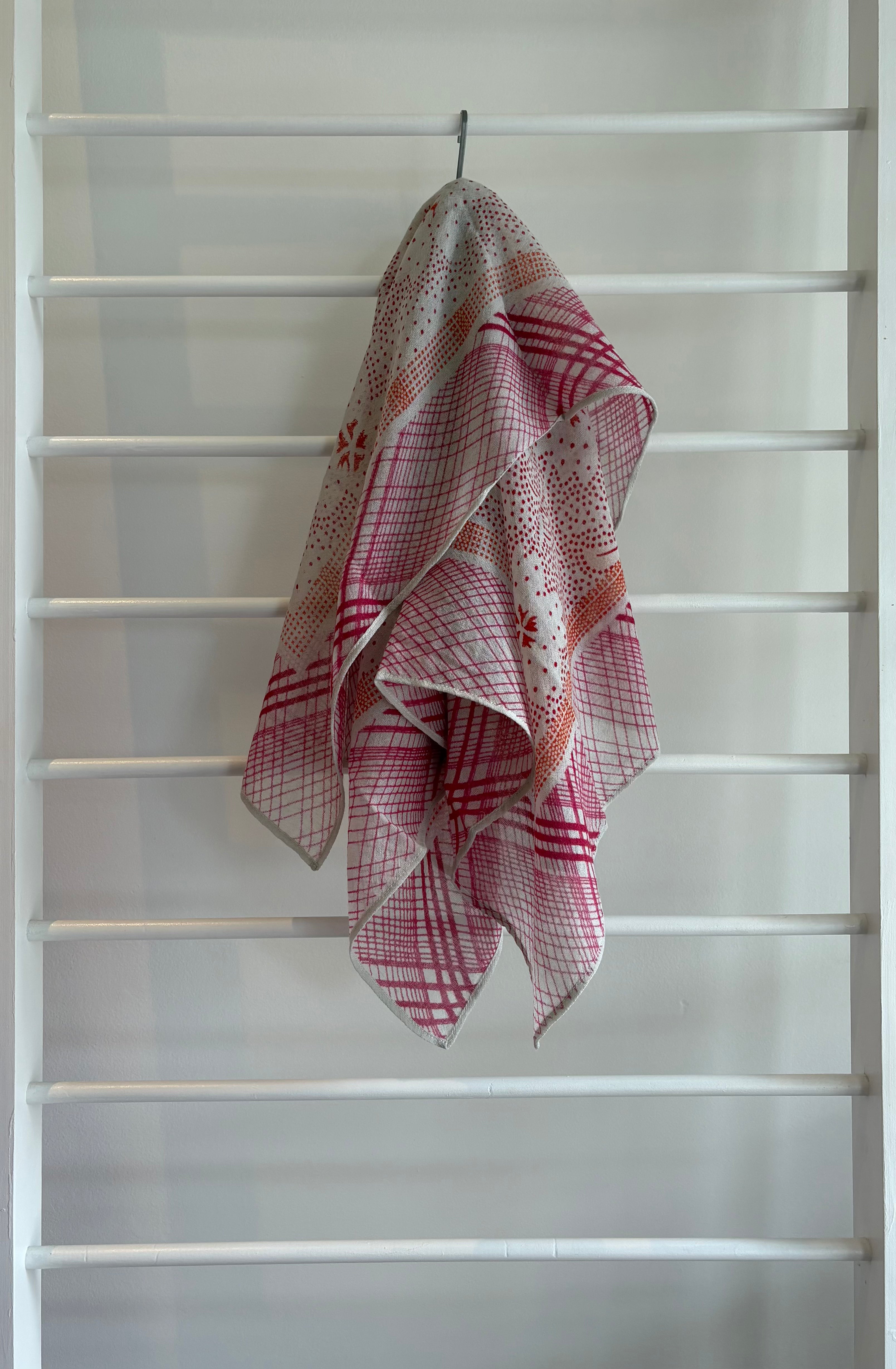 hanging lightweight wool scarf on rack with red, orange and white design.