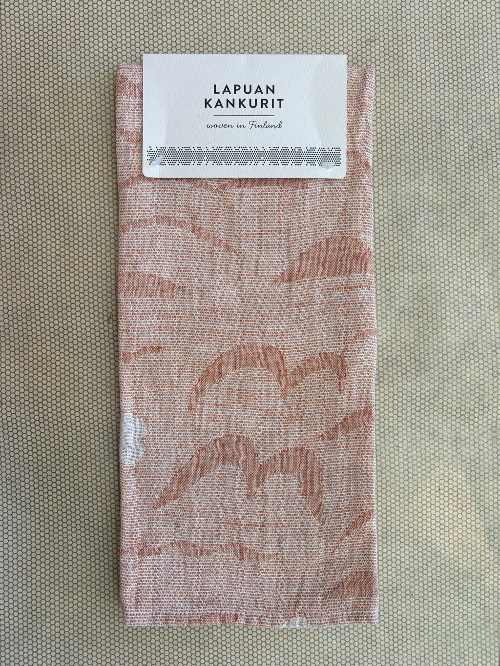 A folded woven fabric item with a white paper label at the top reading 'LAPUAN KANKURIT' and 'woven in Finland,' shown on a textured beige background.
