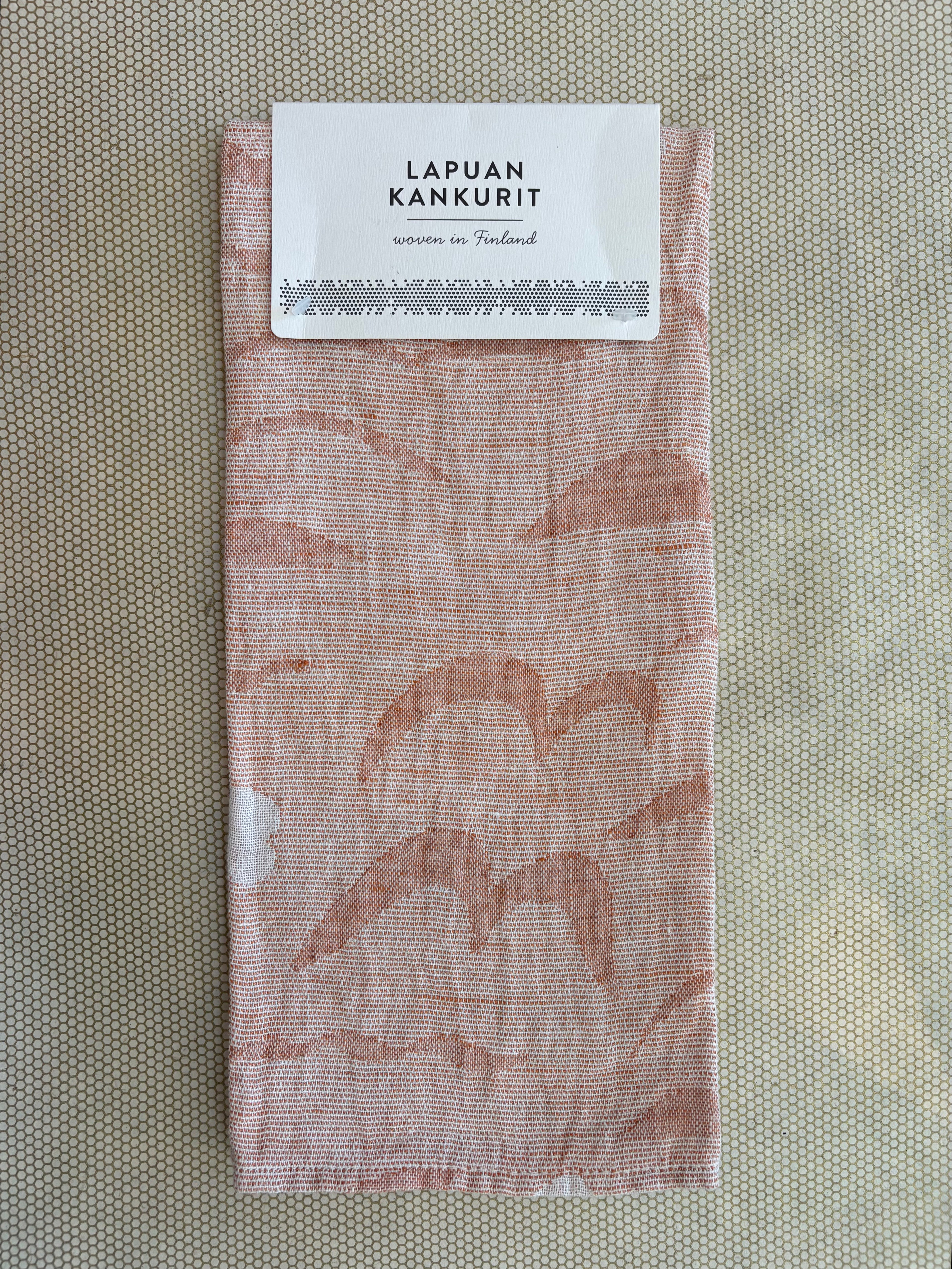 A folded woven fabric item with a white paper label at the top reading 'LAPUAN KANKURIT' and 'woven in Finland,' shown on a textured beige background.