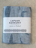 A folded light blue and white patterned woven hand or kitchen towel, wrapped with a white paper label that reads 'LAPUAN KANKURIT' and 'woven in Finland,' placed on a beige patterned surface.