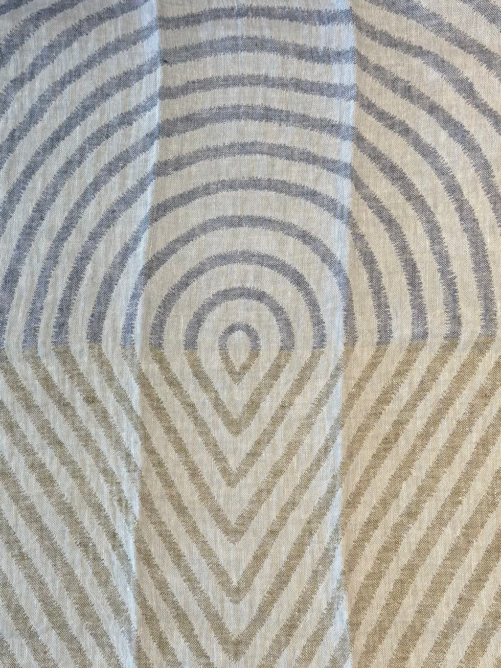 A close-up of a kitchen towel with a geometric pattern of concentric arches and chevrons in muted blue-gray and warm beige and green tones.