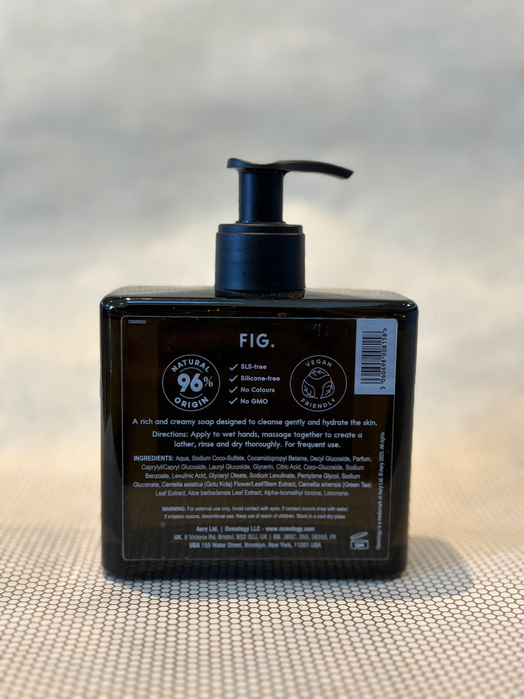 back of liquid soap bottle in Fig scent by Osmology. glass bottle hand soap on neutral background. 