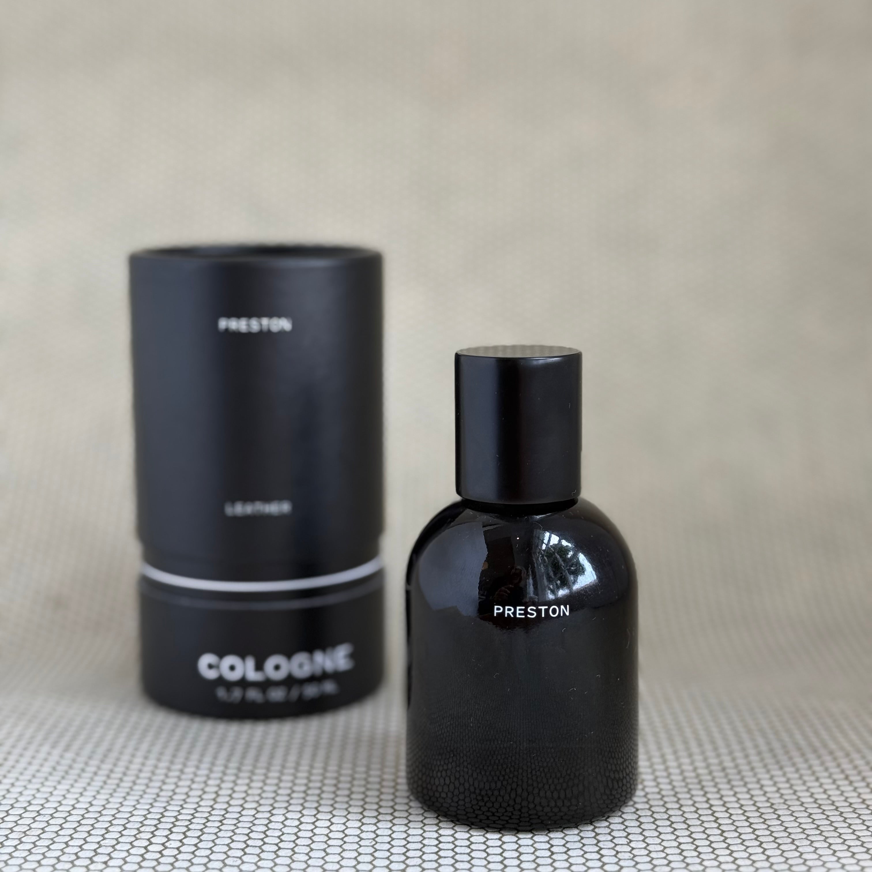 Black Preston leather cologne bottle and packaging on a textured surface with a neutral background