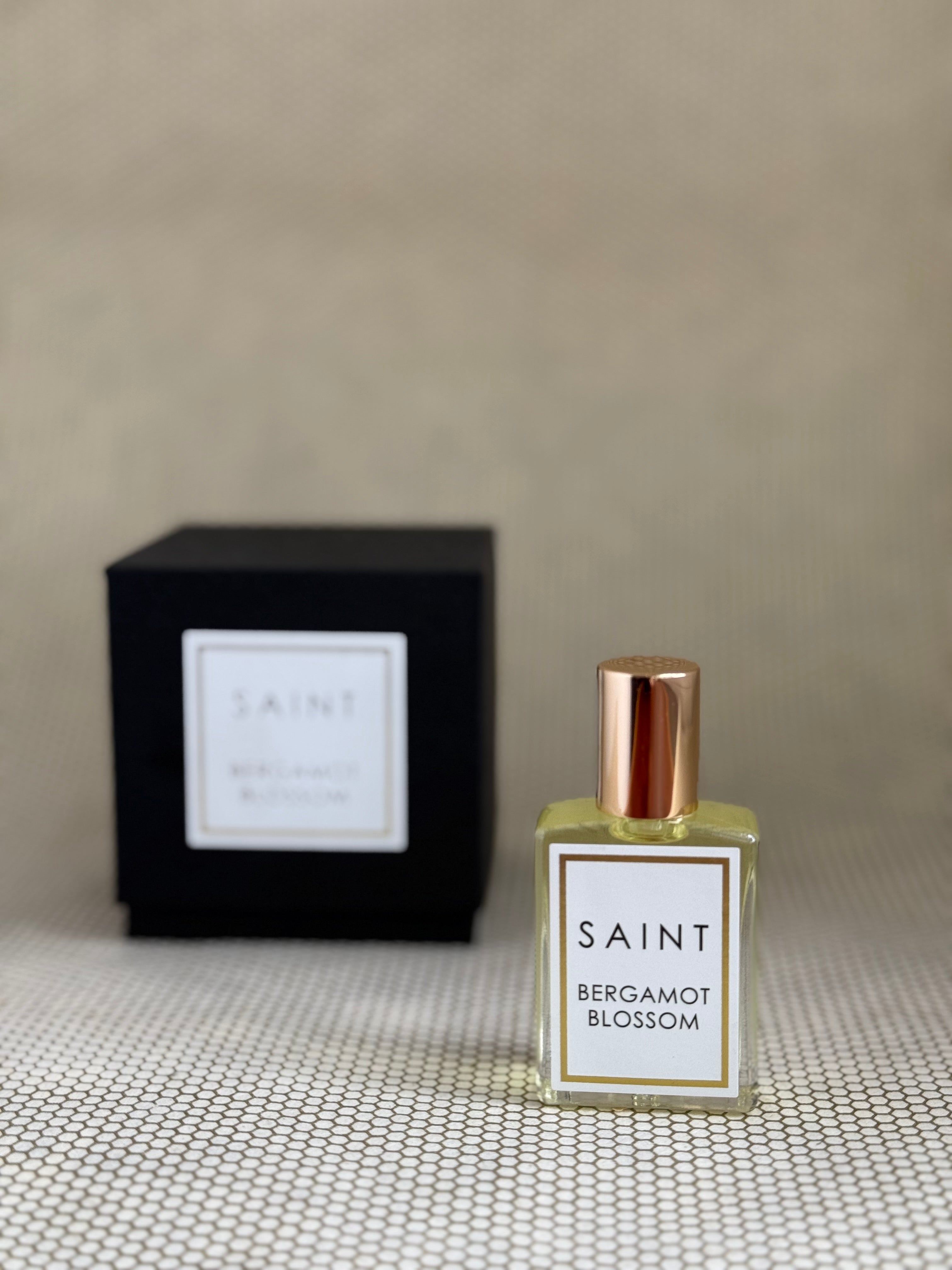 Perfume bottle labeled 'Saint Bergamot Blossom' with a black box in the background on a textured surface.