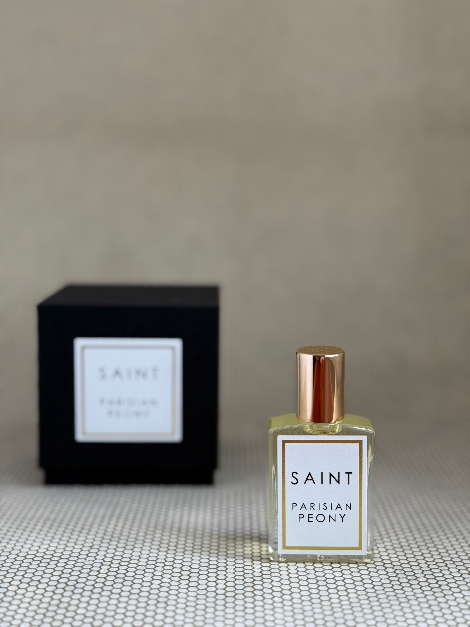 Perfume bottle labeled 'Saint Parisian Peony' with a matching black box on a textured surface.