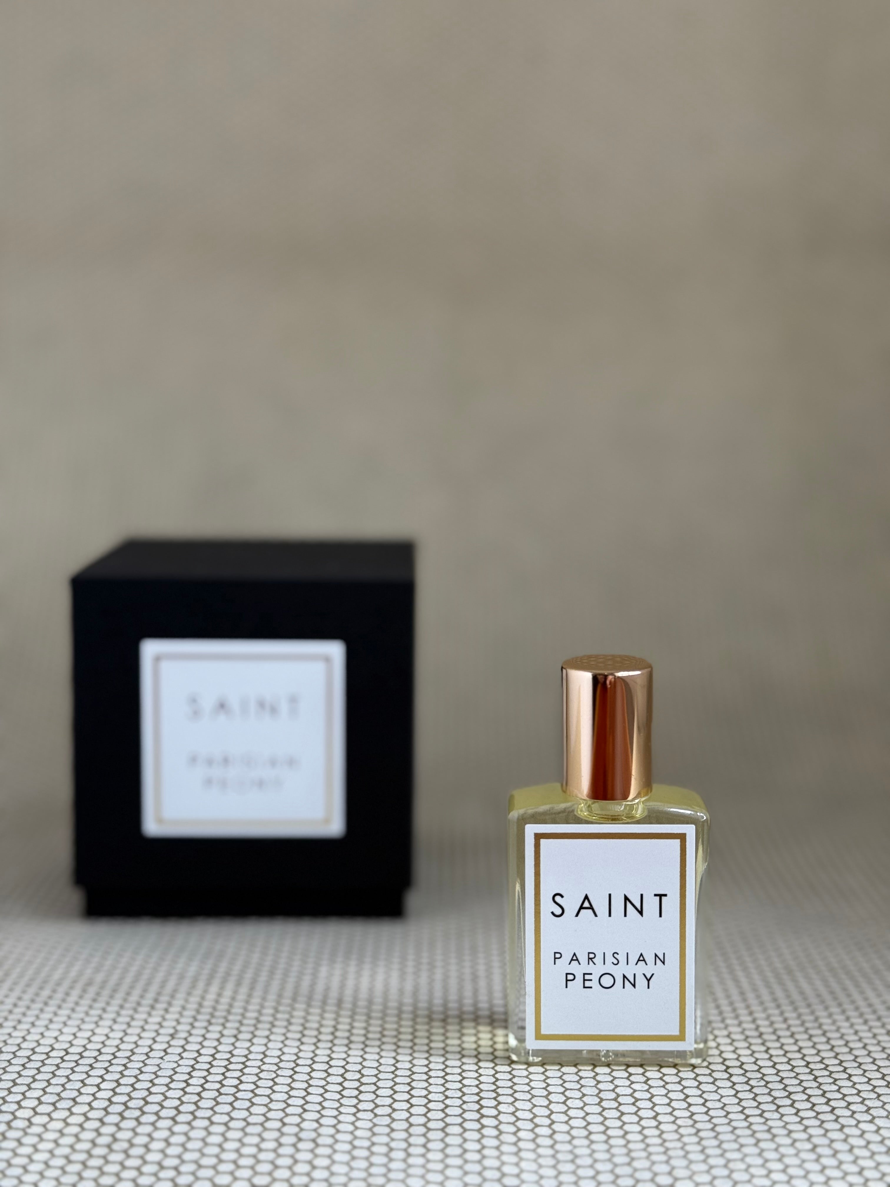 Perfume bottle labeled 'Saint Parisian Peony' with a matching black box on a textured surface.